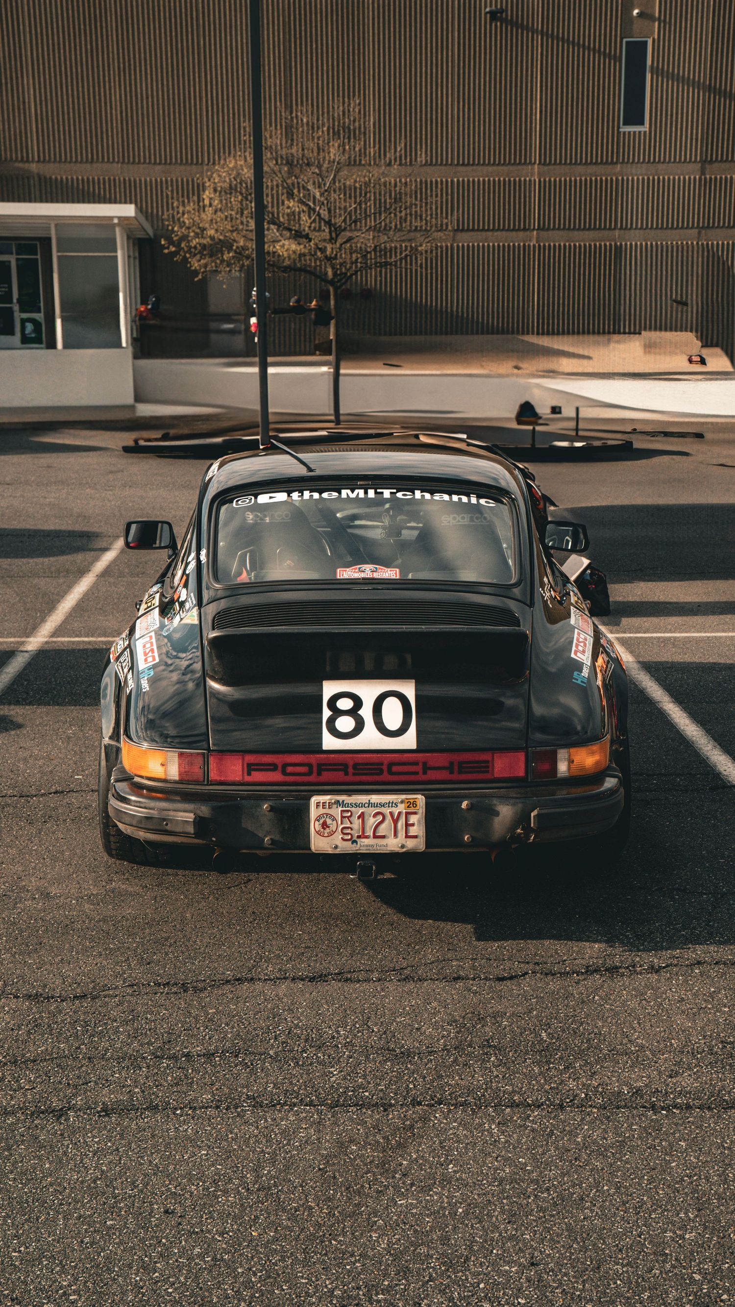 Black Porsche 911 race car with number 80 parked in a lot with vintage styling and racing modifications.