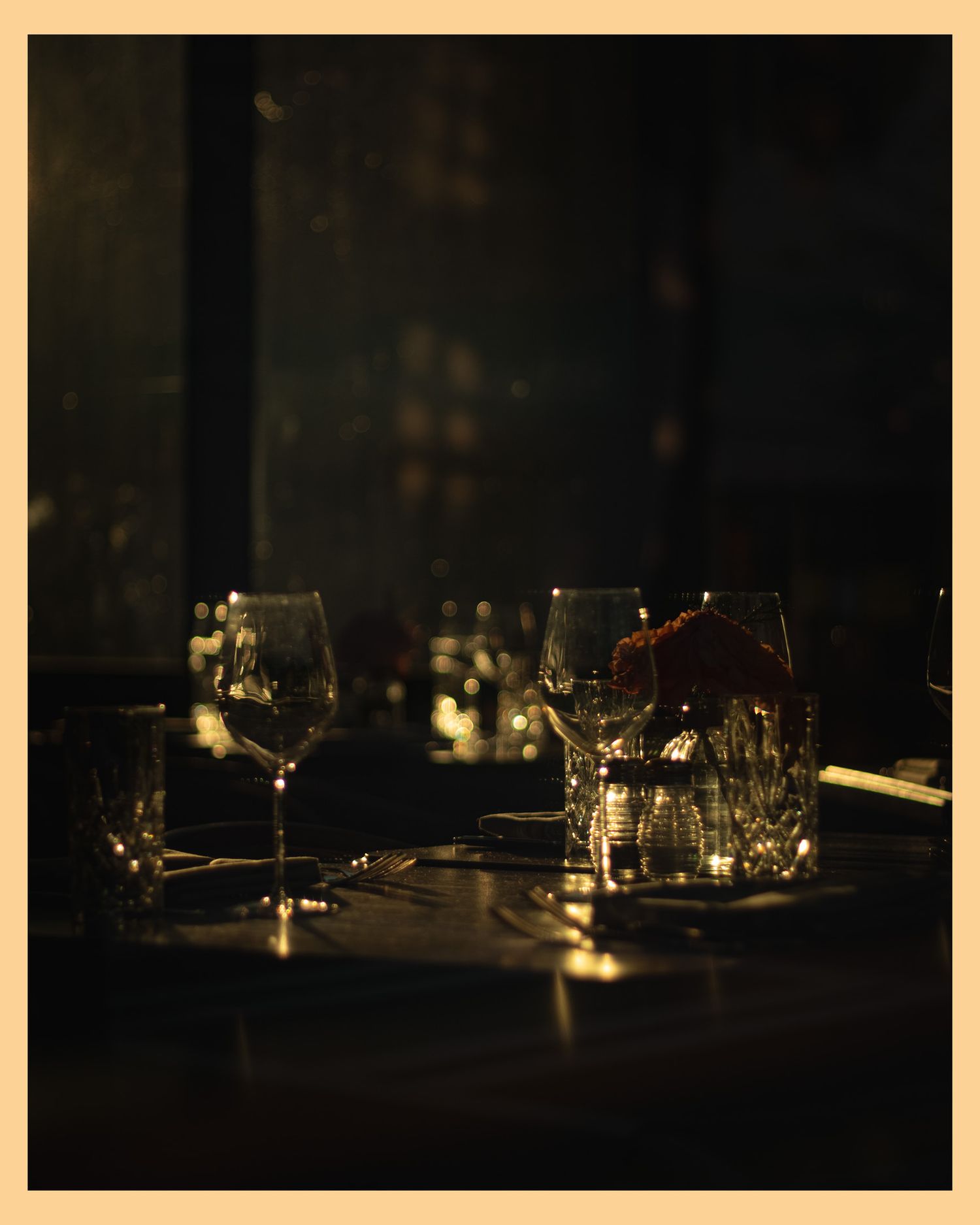 Moody restaurant table setting with wine glasses in dim lighting.