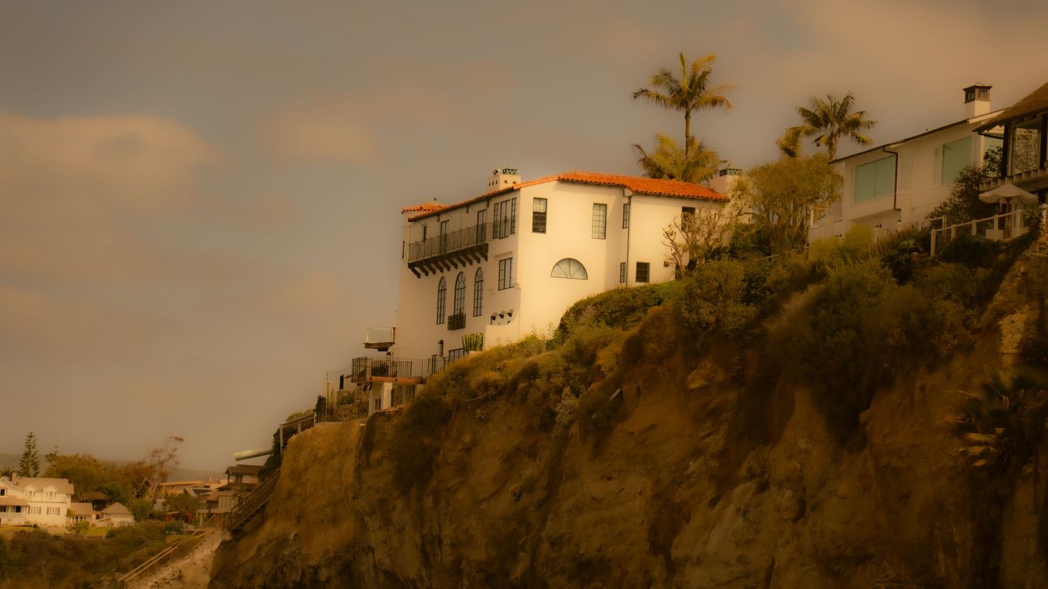 White house perched dramatically on an oceanside cliff during golden hour.