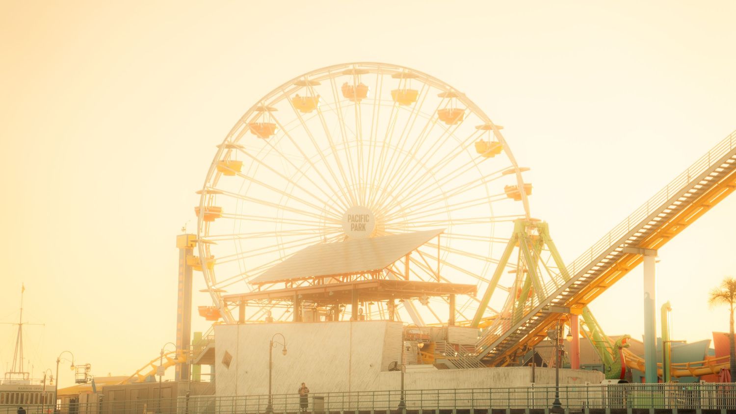 Misty morning view of Pacific Park's Ferris wheel and roller coaster through golden sunlight.