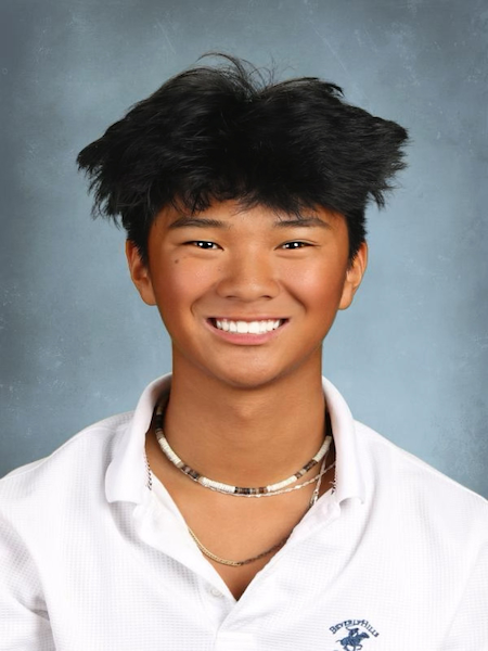 Student portrait against grey background wearing white collared uniform shirt and necklace.