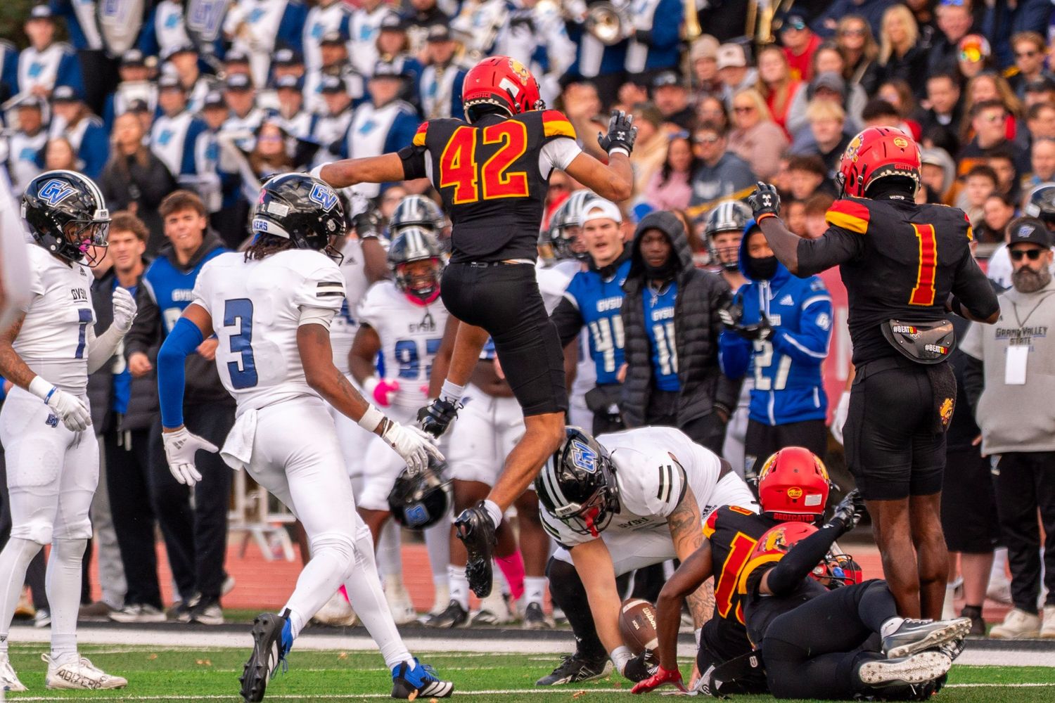 Football player in orange jersey number 42 leaps high during game action with crowd in background.