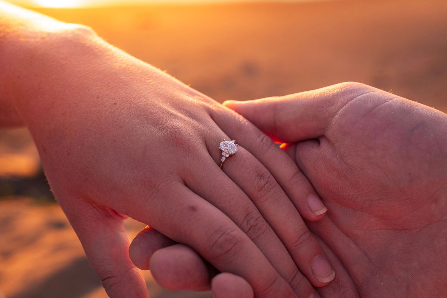 Two hands reaching out to hold each other against a warm, golden sunset background.