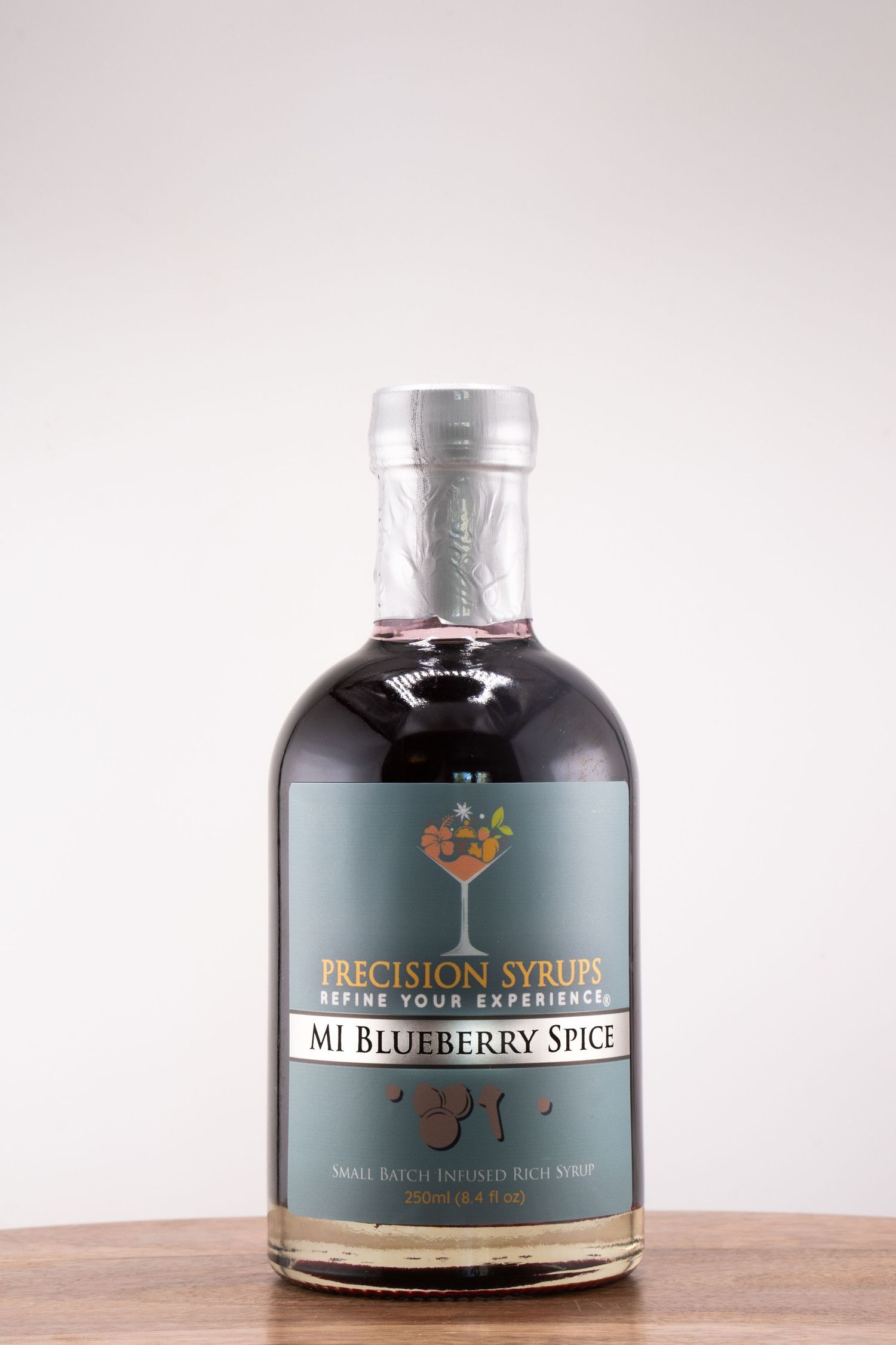 A bottle of MI Blueberry Spice Precision Syrup on a wooden surface against a light background.