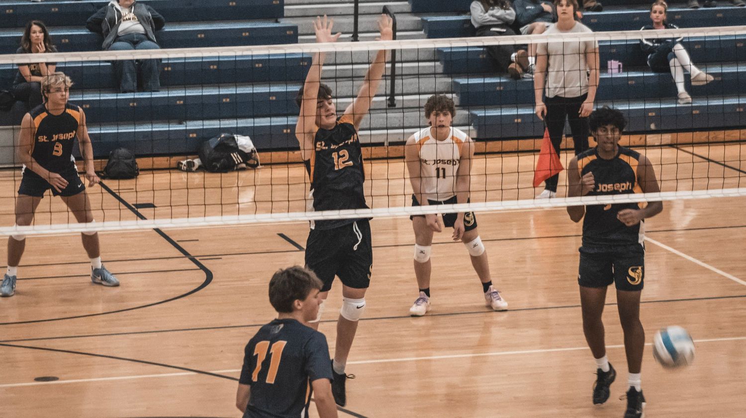 Teams engaged in volleyball match with players positioned on both sides of net.