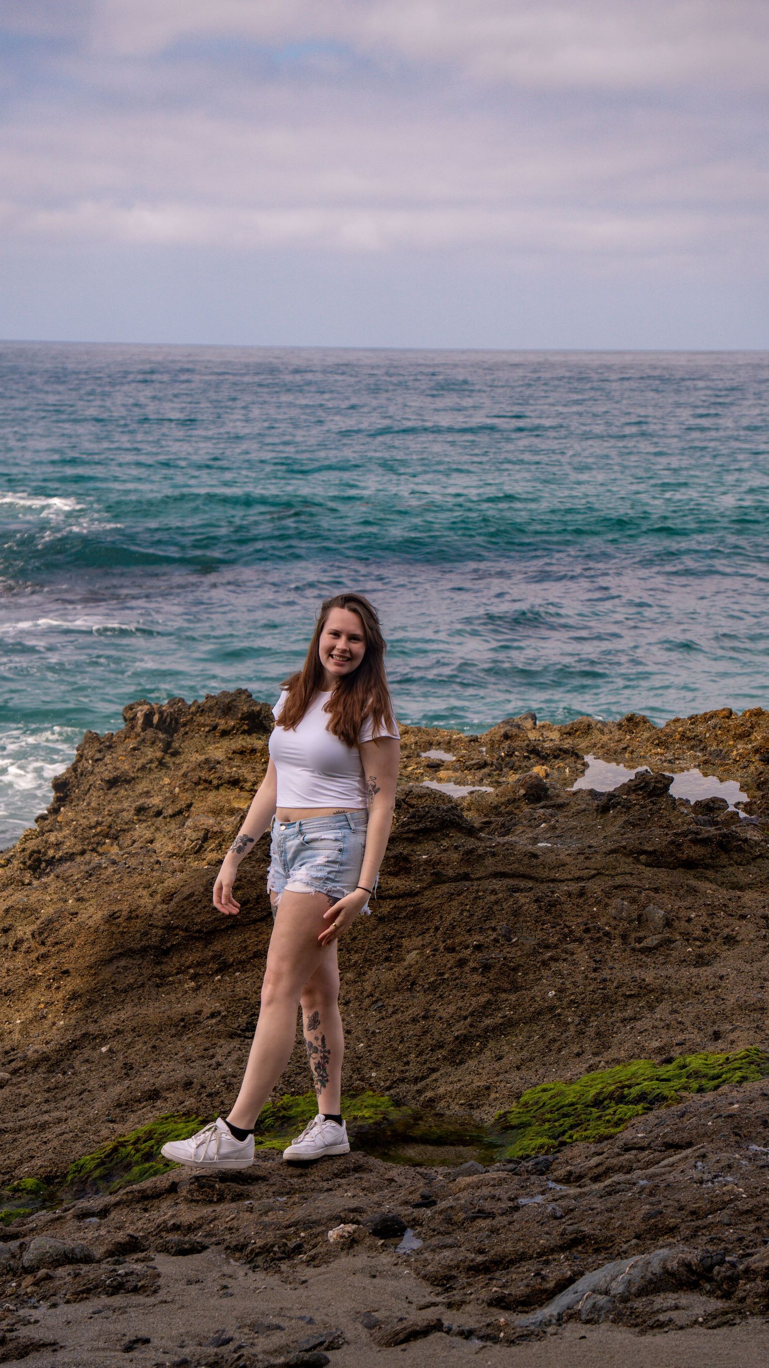 Person exploring rocky oceanside terrain in white sneakers and casual clothing.