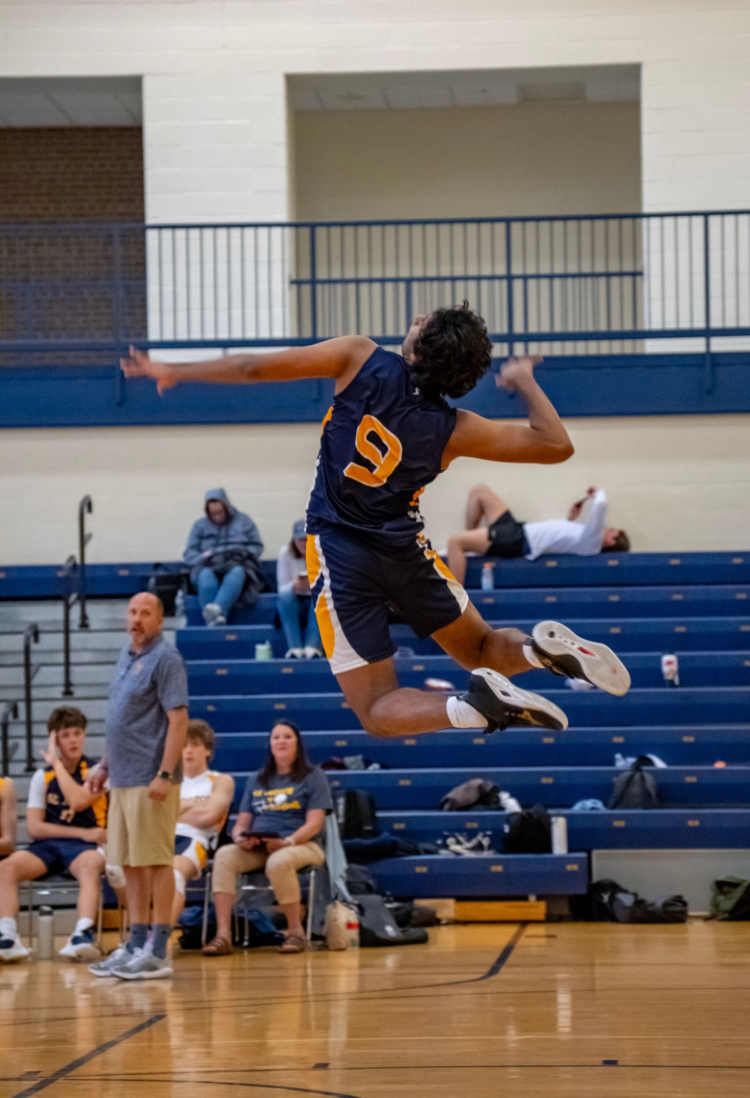 A volleyball player in navy jersey number 9 leaps high to spike the ball during a match.