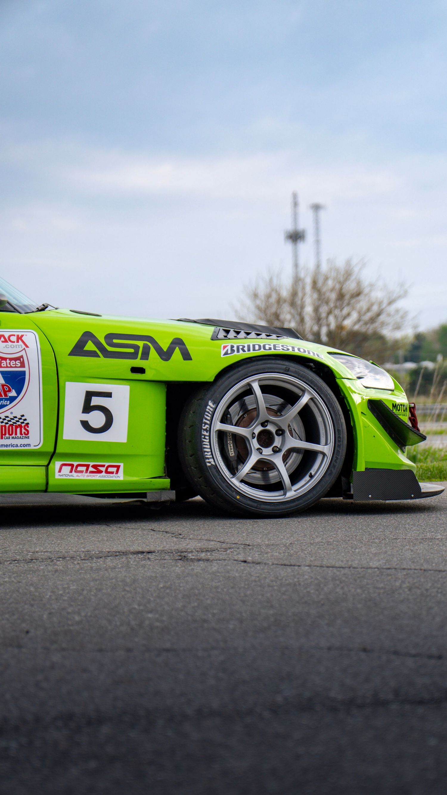 Close-up of a green race car's wheel and side panel showing racing number 5 and sponsor logos.