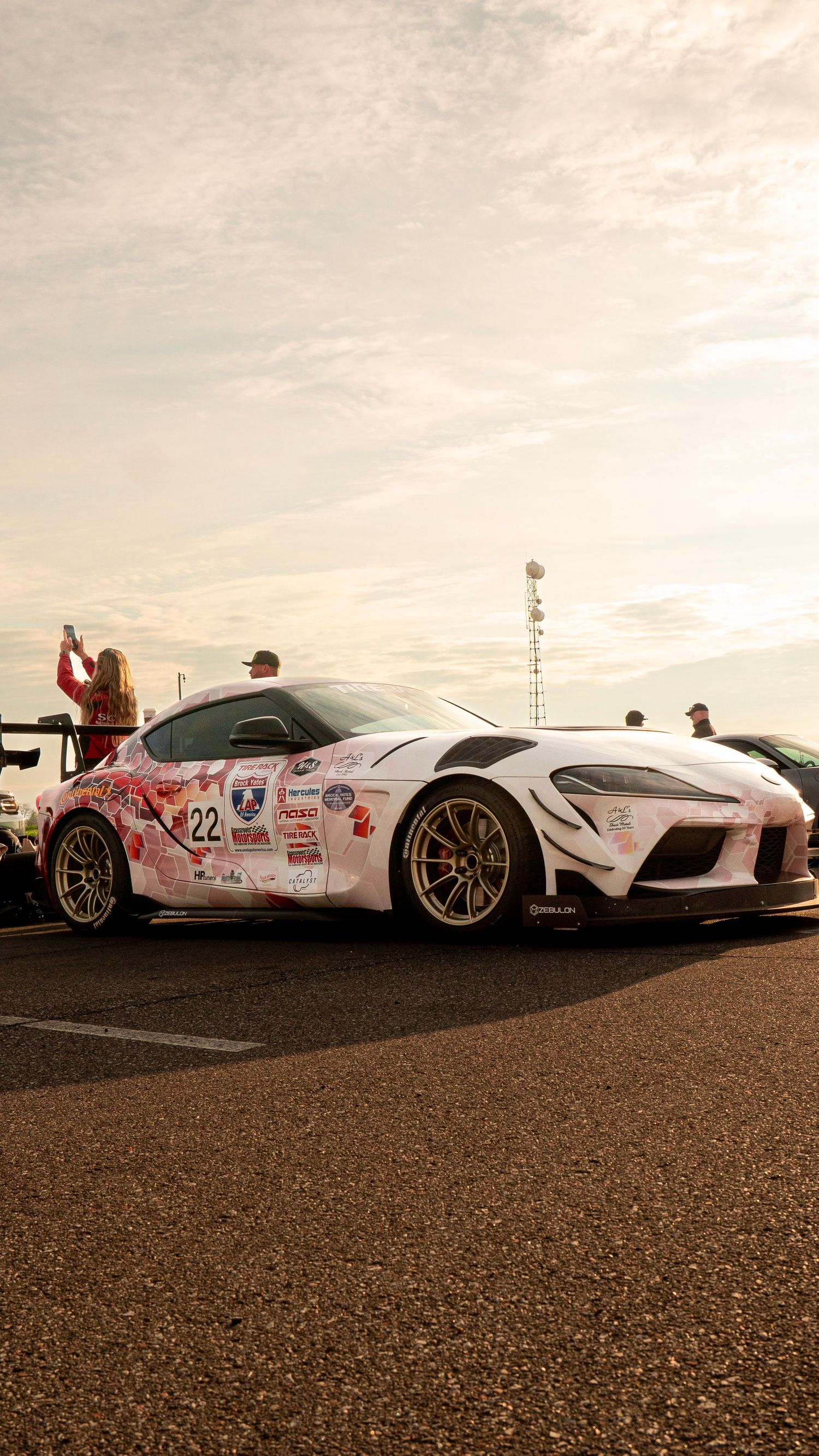 White Toyota Supra with racing livery and gold wheels photographed at sunset.