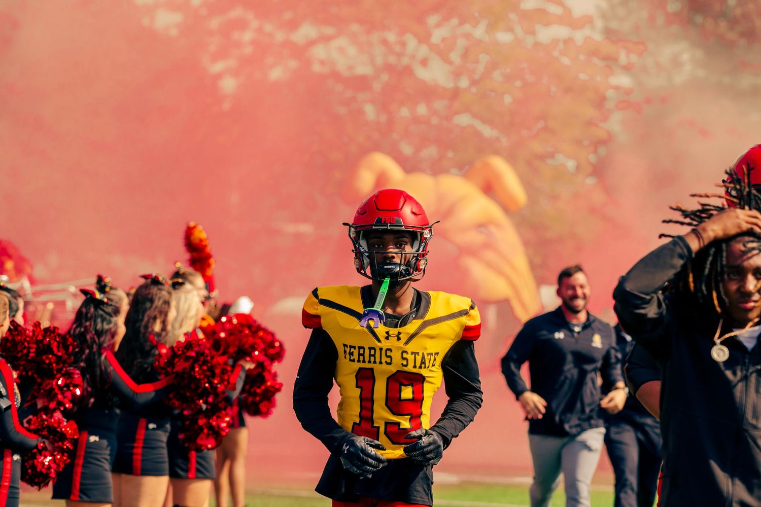 Football players in yellow and red uniforms compete during a match with spectators in the background.
