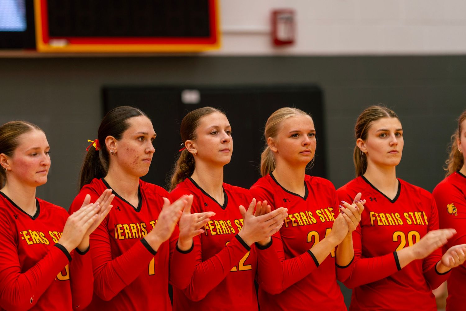 Row of volleyball players in red uniforms standing together during pre-game ceremonies.