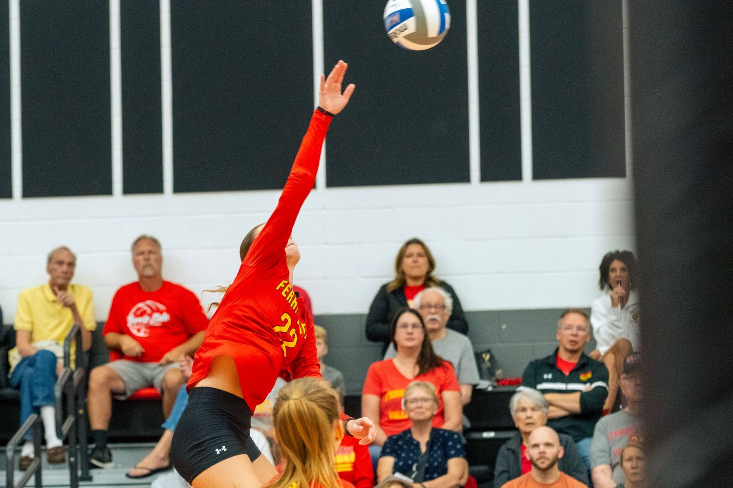Indoor volleyball match showing players in red uniforms positioning for a play at the net.