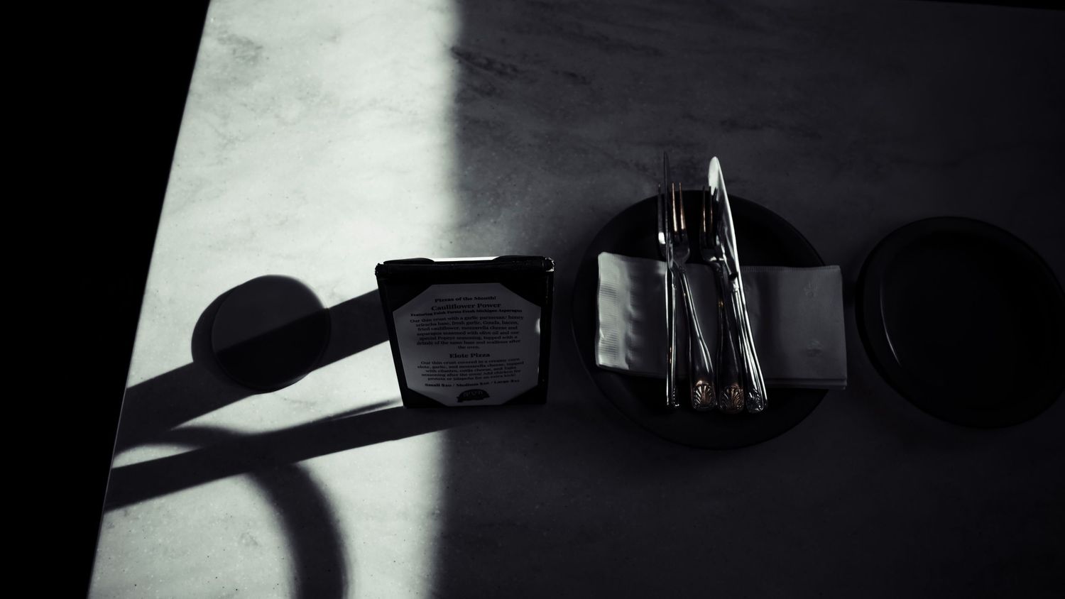 A dramatic black and white composition of sunglasses casting a shadow on a white surface next to writing utensils.