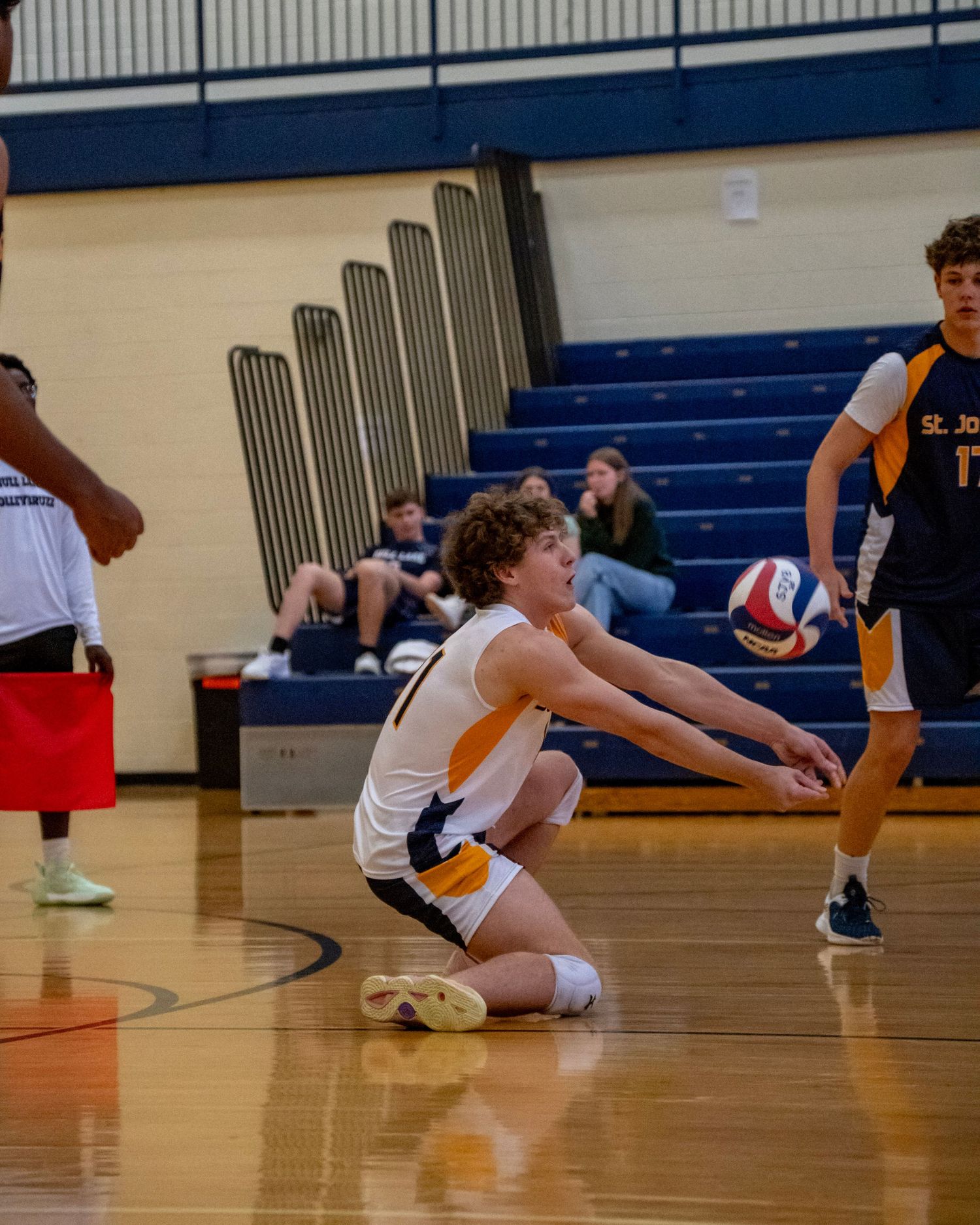 Players diving and stretching on the gymnasium floor during volleyball practice.