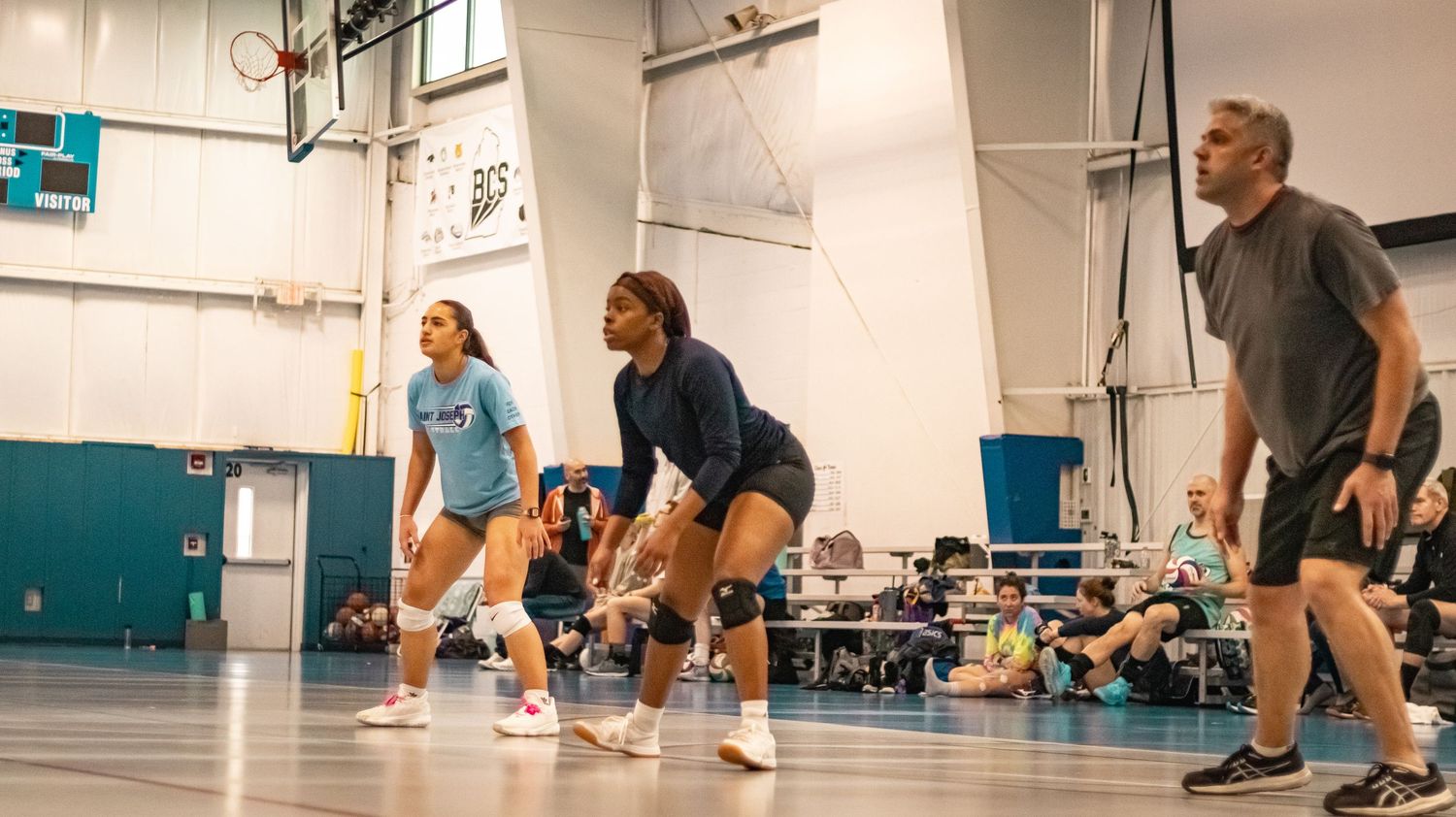 Players in athletic gear ready their positions during indoor volleyball practice.