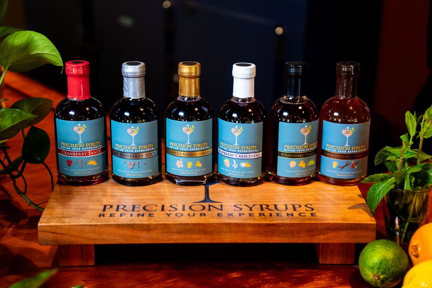 Six bottles of premium spirits displayed on a wooden serving board with fresh citrus fruits and herbs.
