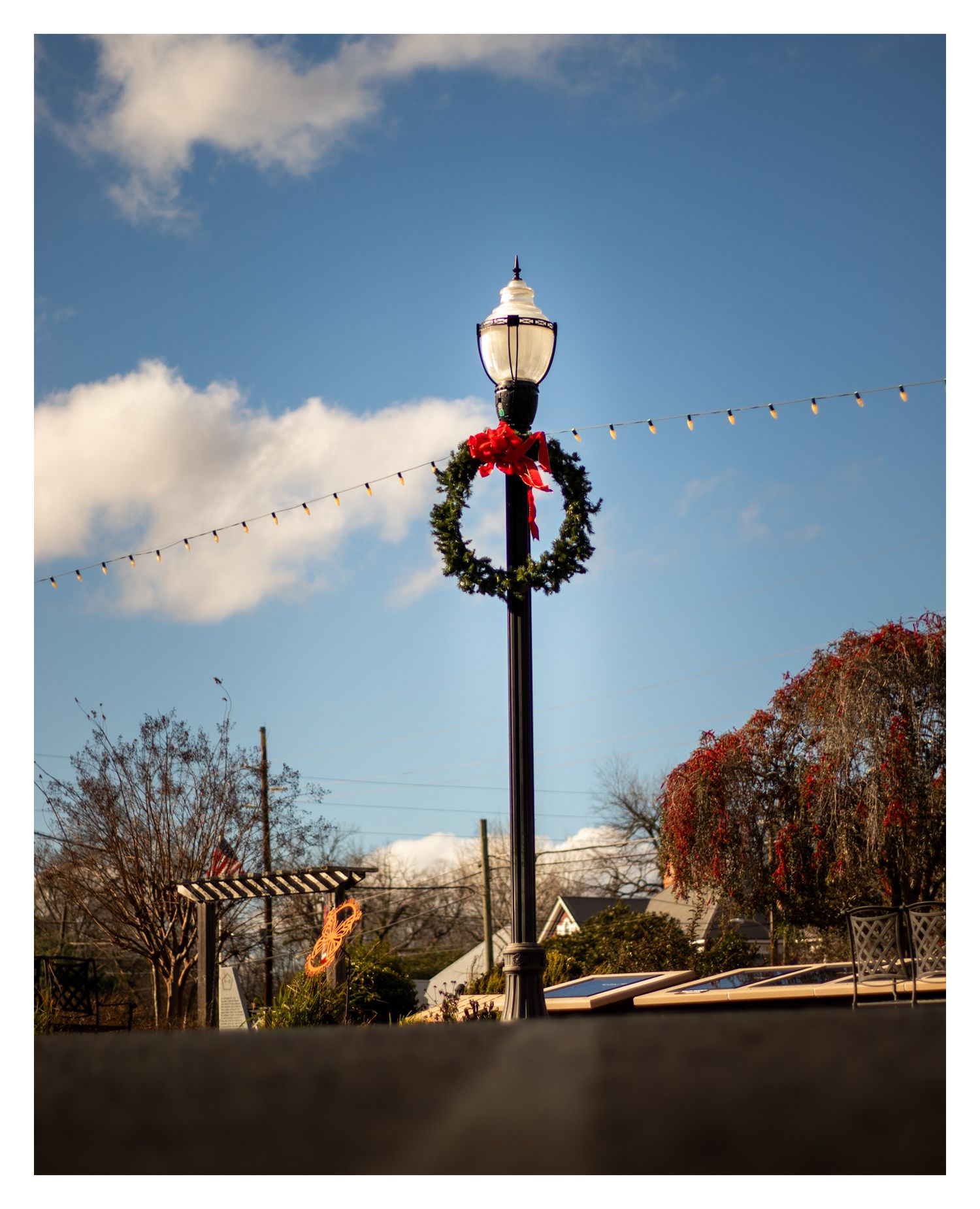 Traditional lamp post decorated with holiday wreath and string lights against blue sky.