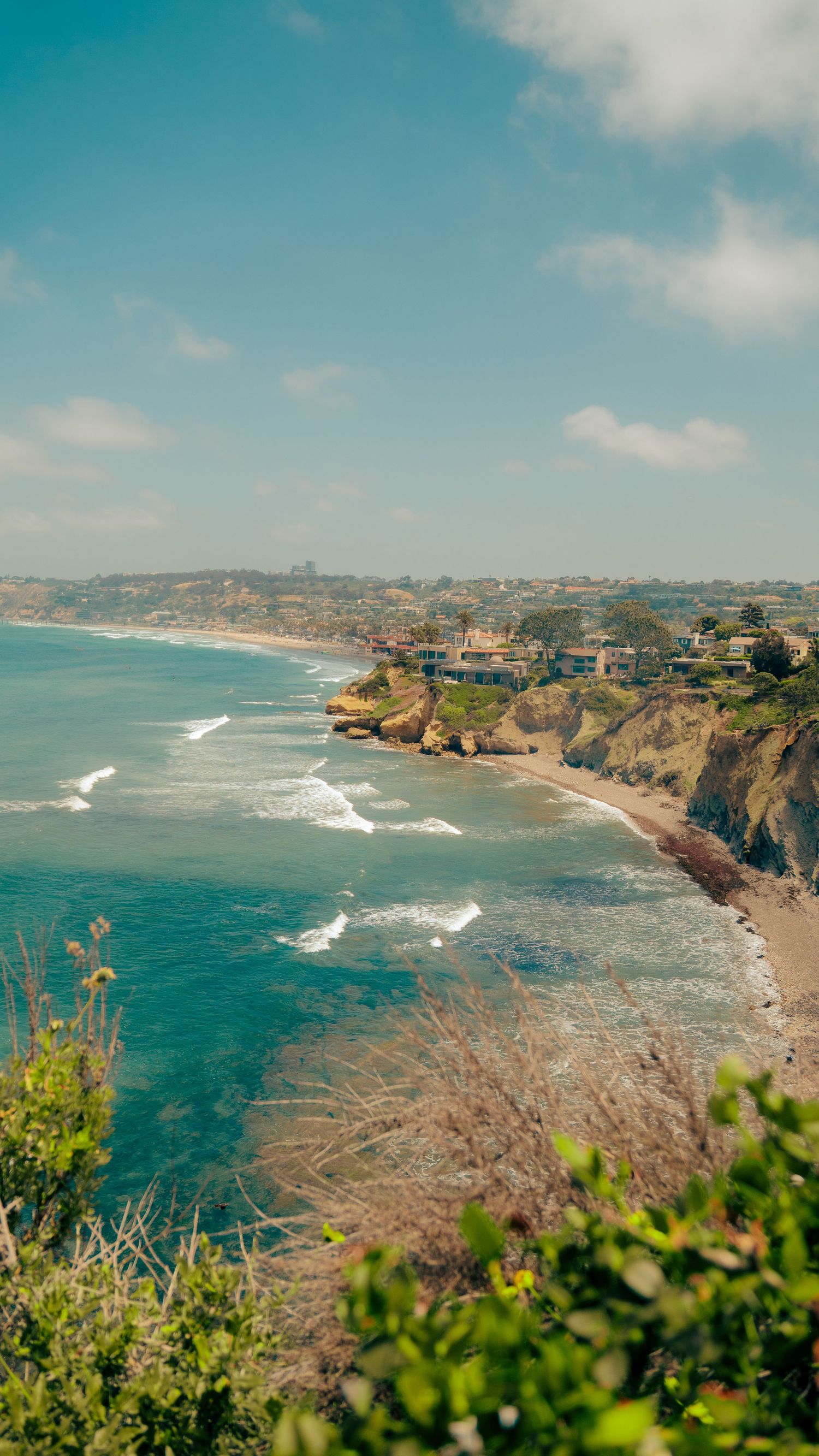 Scenic coastal view of turquoise ocean waters meeting rugged cliffs with houses perched along the California coastline.