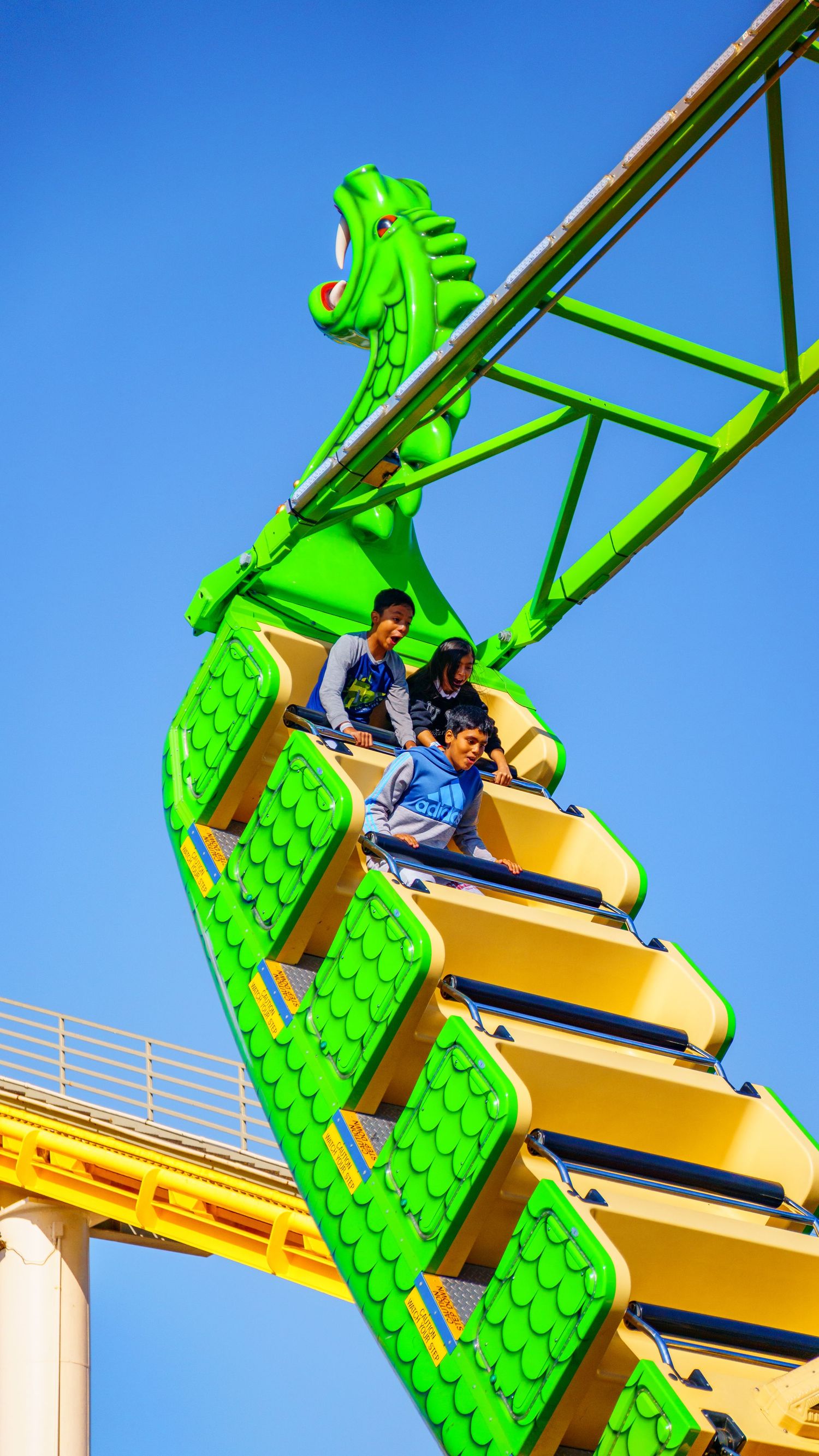 Bright green dragon-themed roller coaster car with yellow seats against blue sky.