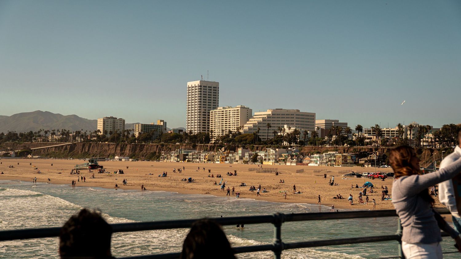 Coastal cityscape panorama showing beach, buildings and mountains under clear blue skies.