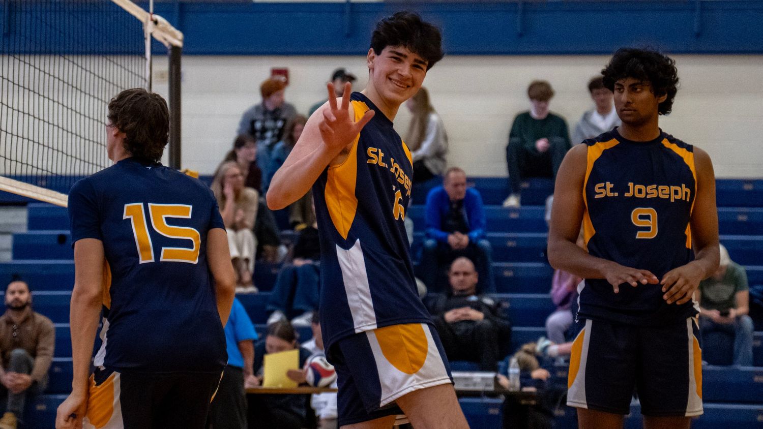 High school volleyball players in navy and gold uniforms compete during an indoor match.