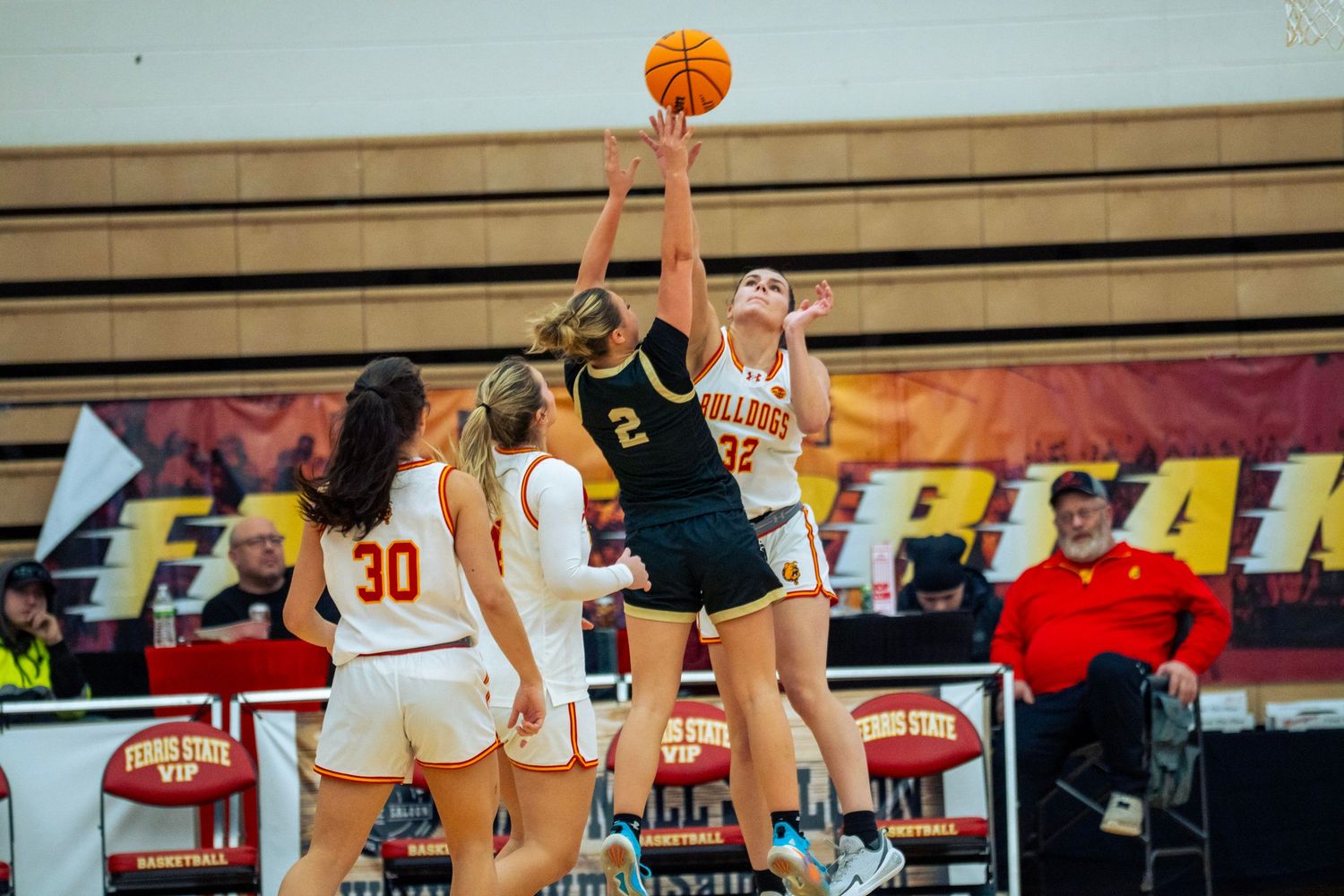 Basketball players jump to grab a rebound during an intense game on a wooden court.
