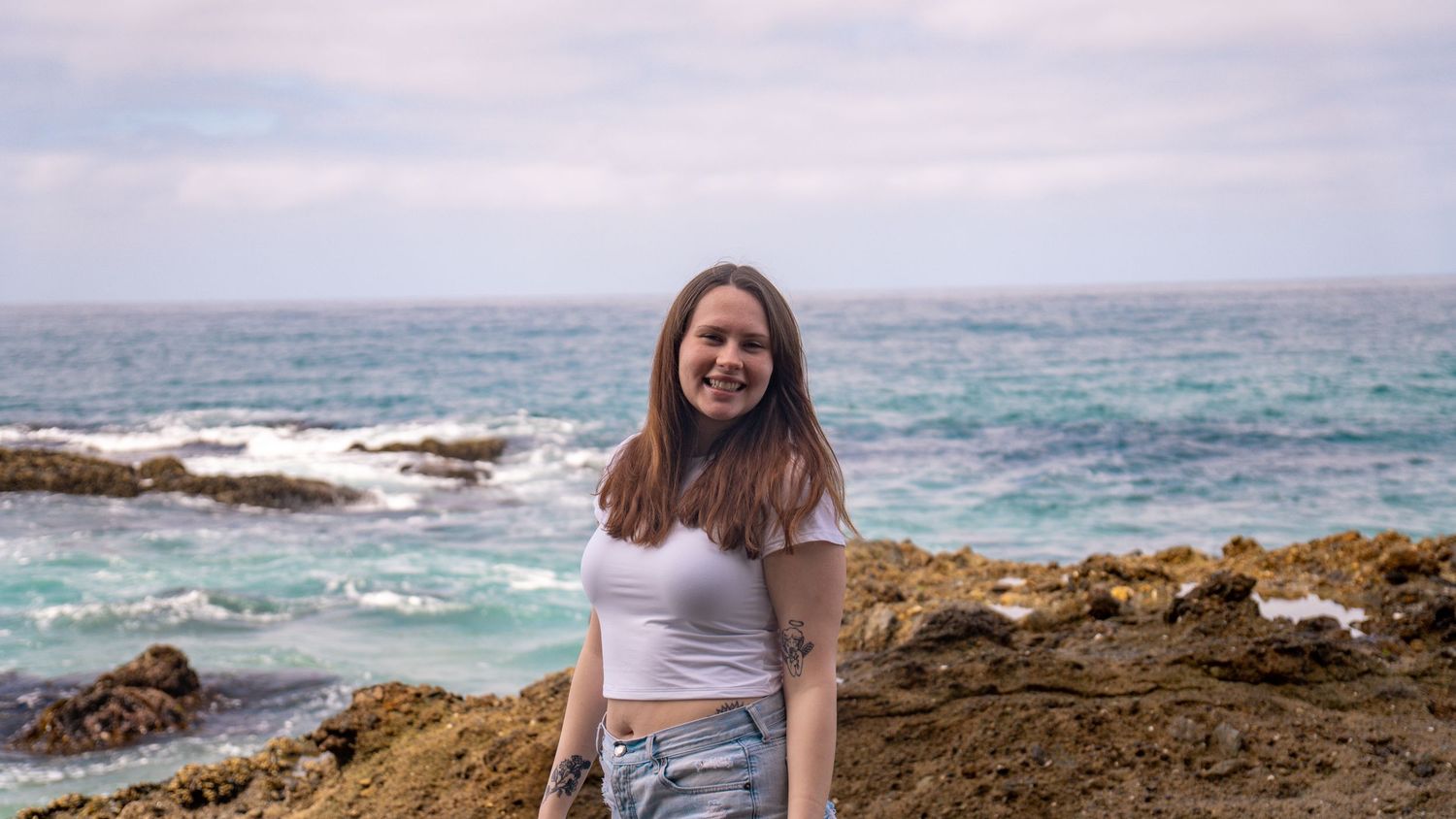 Casual seaside portrait with rocky coastline and turquoise waters in background.