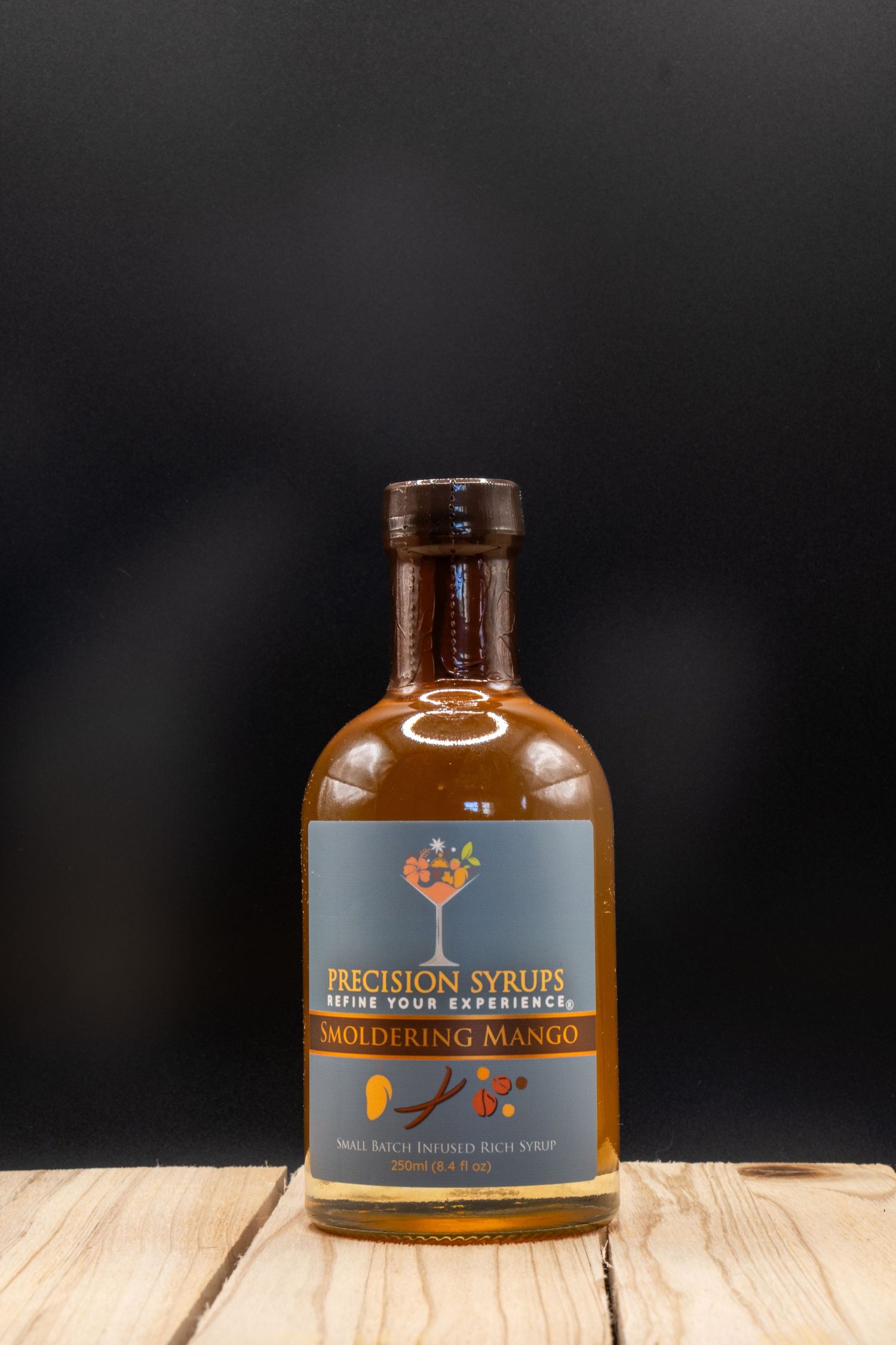 Precision Syrups cocktail mixer bottle with blue label on wooden table against dark background.