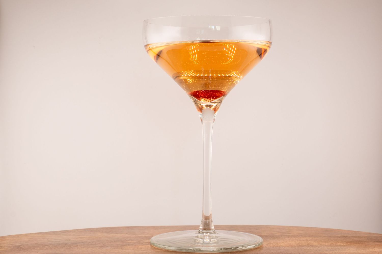 Close-up shot of a coupe glass containing a peachy-pink cocktail on a wooden surface with warm lighting.