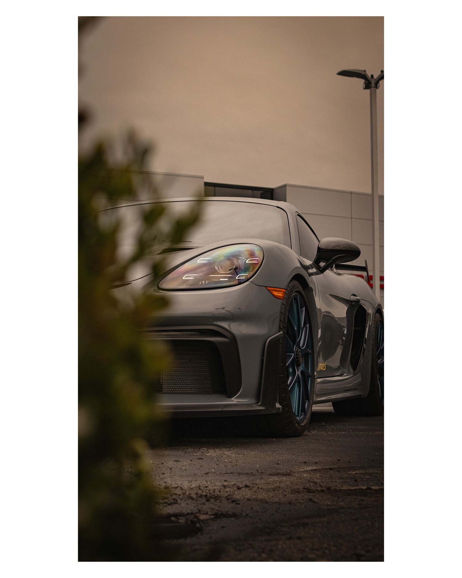Close-up detail shot of gray Porsche GT3 front headlight and fender with blue wheels.