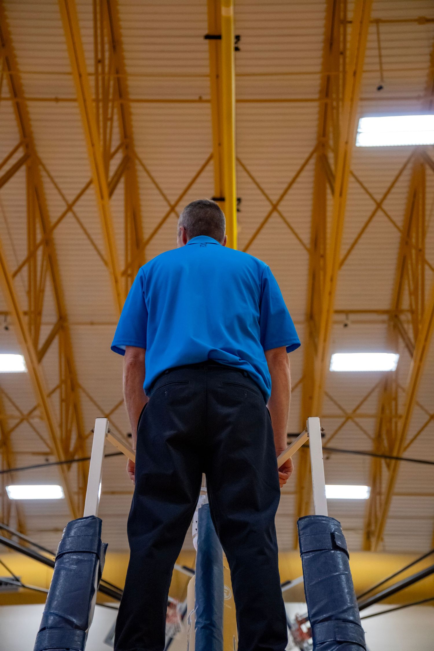 Officials in blue uniforms watch over a volleyball match from an elevated position.