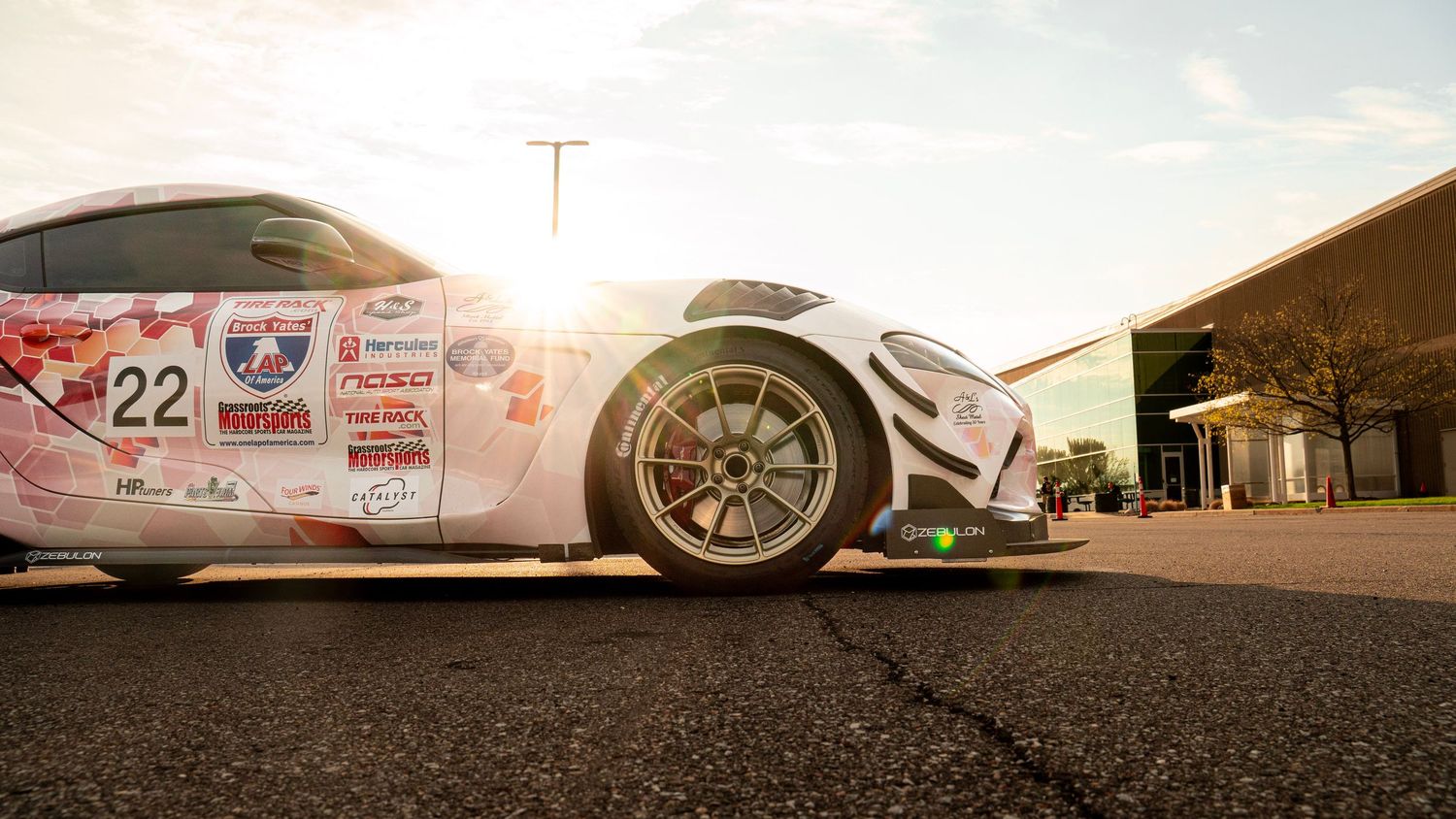 Panoramic low angle view of race car on asphalt with dramatic sunset lighting.