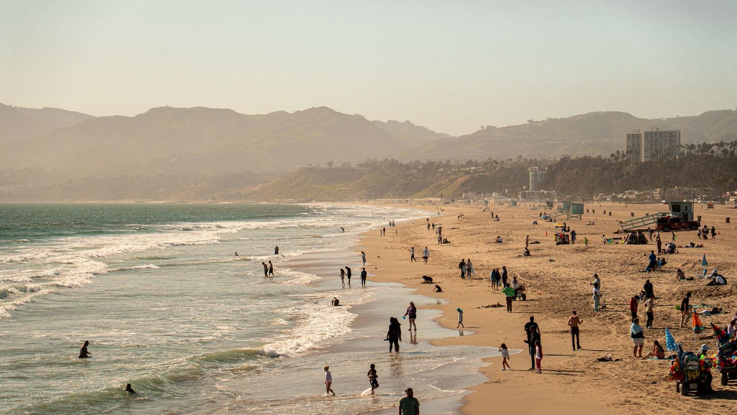Panoramic view of a California beach with mountains and people enjoying the coastline.