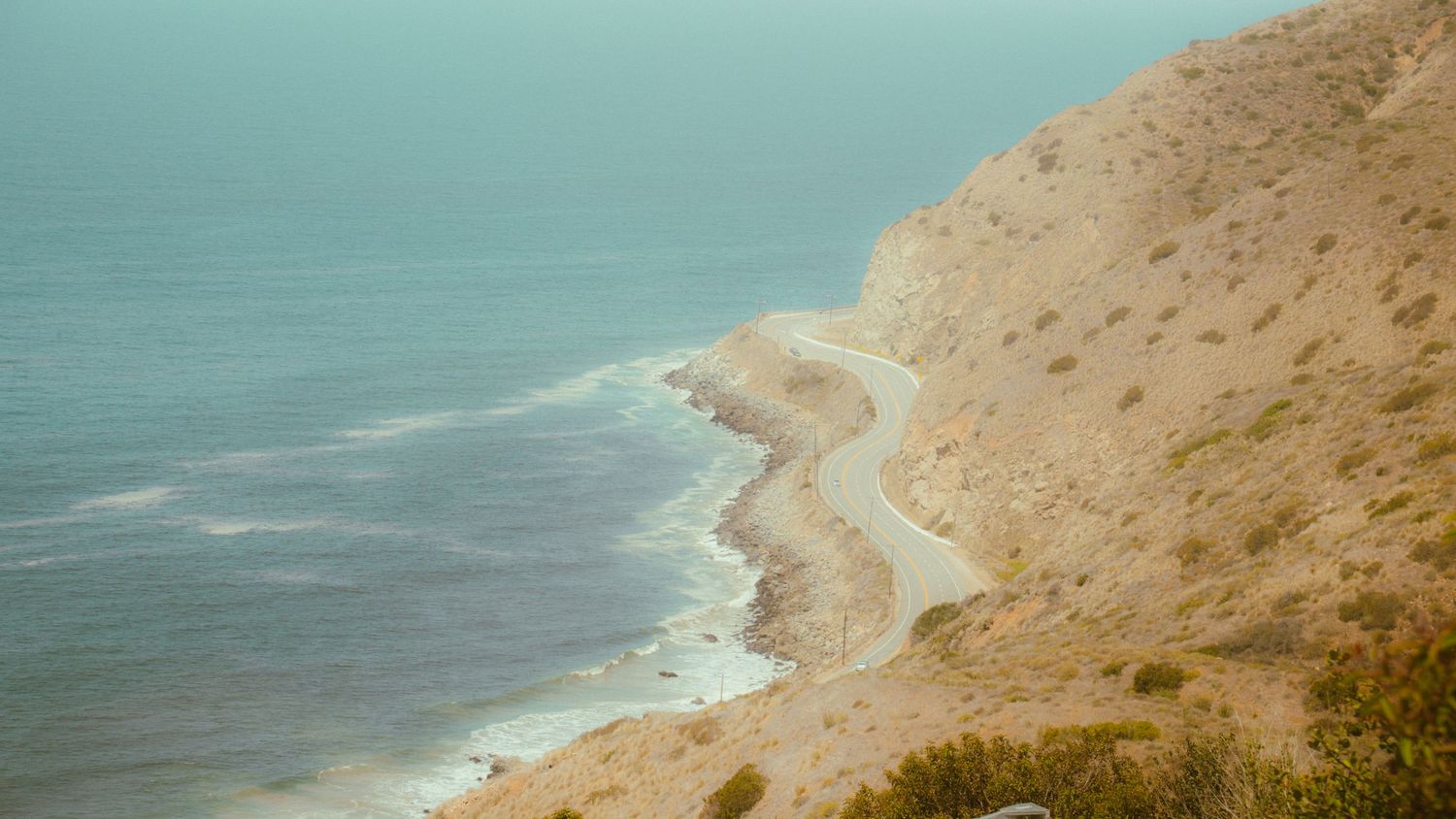 Aerial view of a winding coastal road nestled between steep cliffs and the blue ocean.