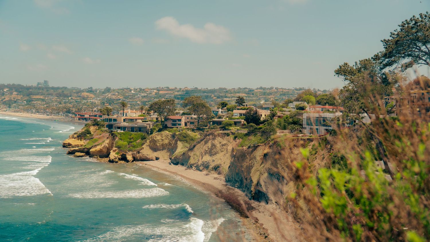 Curved coastline with houses nestled on green cliffs above turquoise ocean waters.