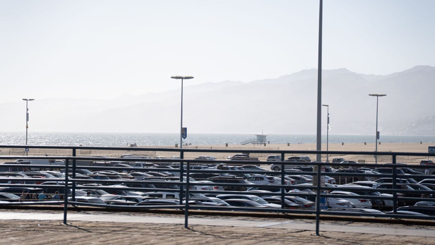 Empty parking lot with mountain silhouettes and lamp posts in misty morning light.