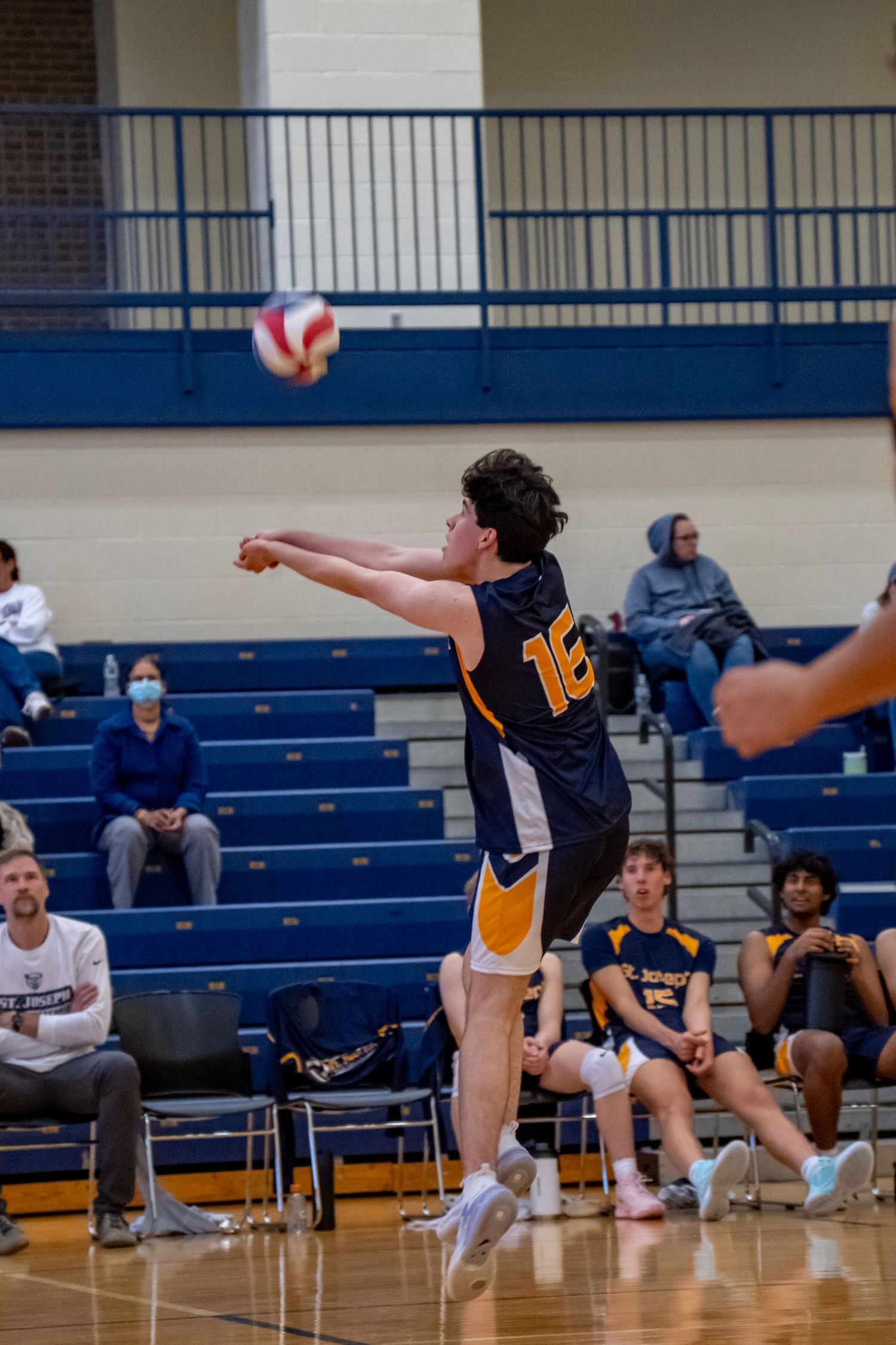 Volleyball player in navy jersey number 16 jumps to serve the ball.
