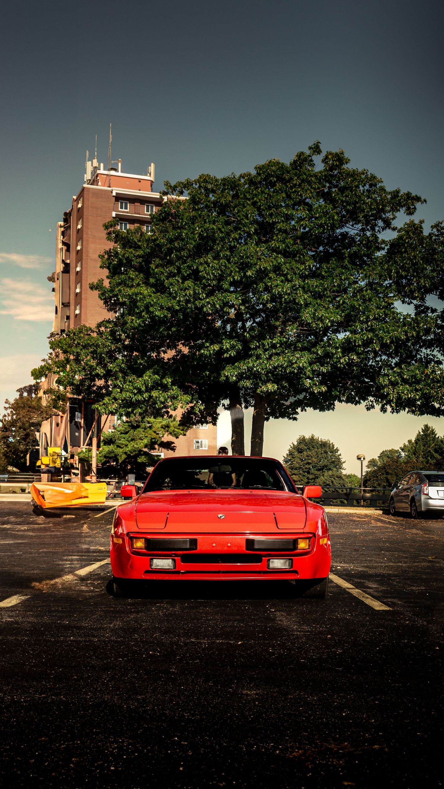 Classic red Porsche photographed in parking lot with vintage apartment building in background.