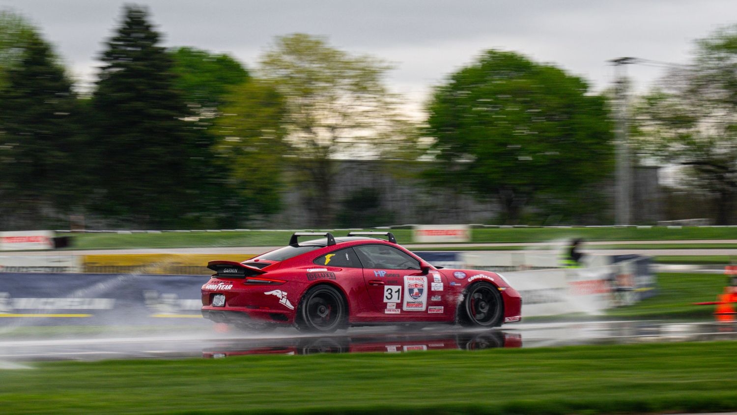 Red race car sliding sideways through wet racing corner.