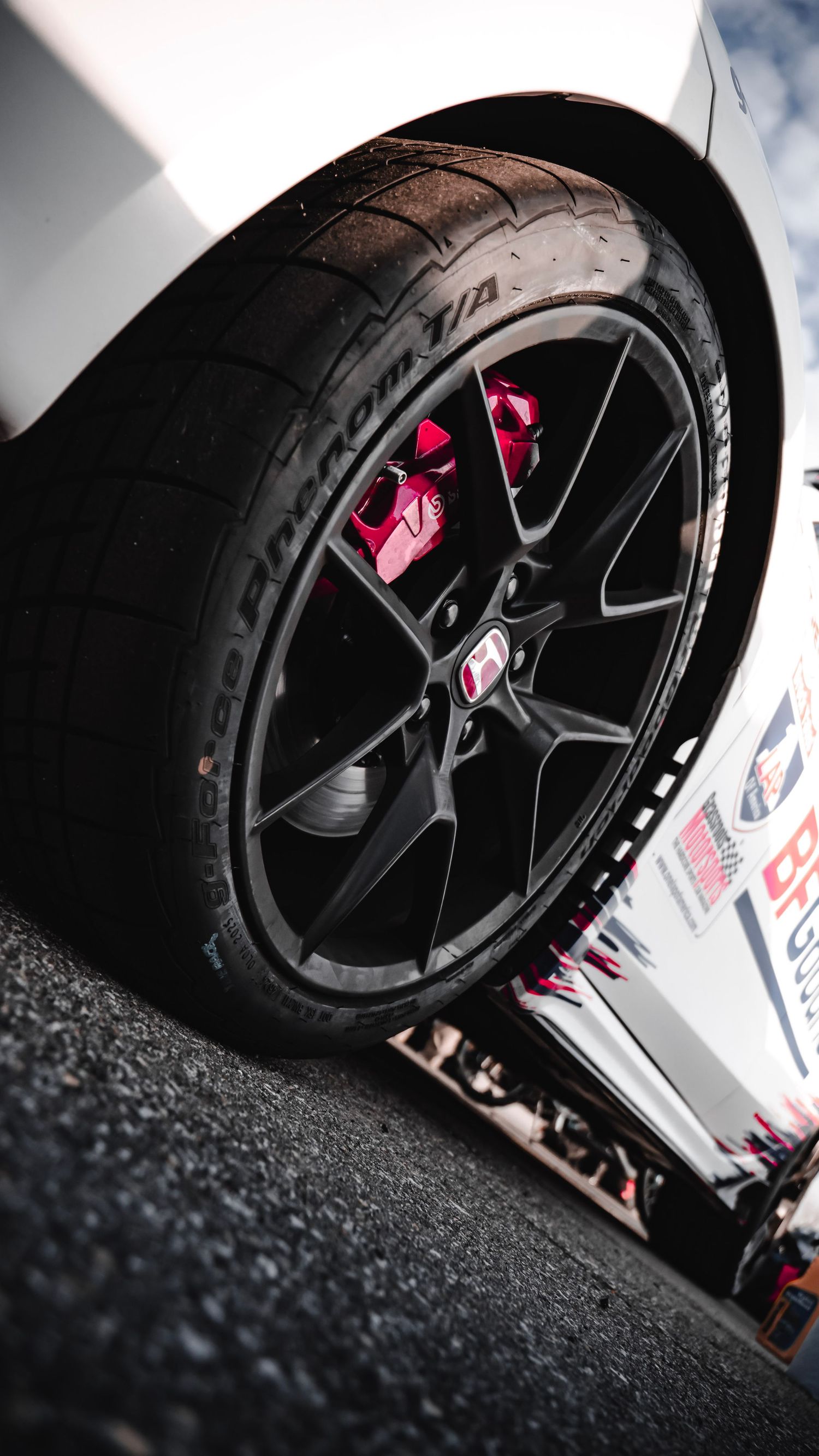 Close-up of black racing wheel with red brake caliper and performance tire.