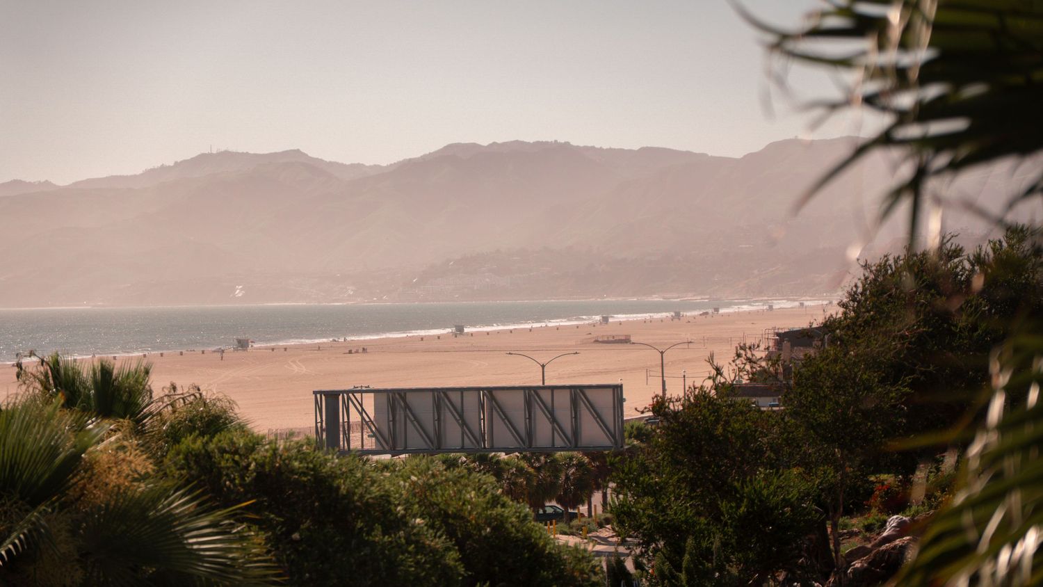 Beachfront view with mountains and palm trees in warm afternoon light.