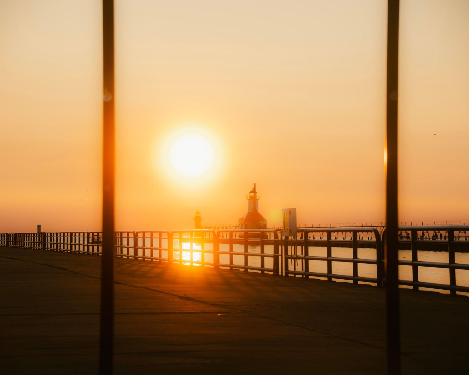 Dramatic sunset silhouettes St. Joseph lighthouse and pier through vertical poles.