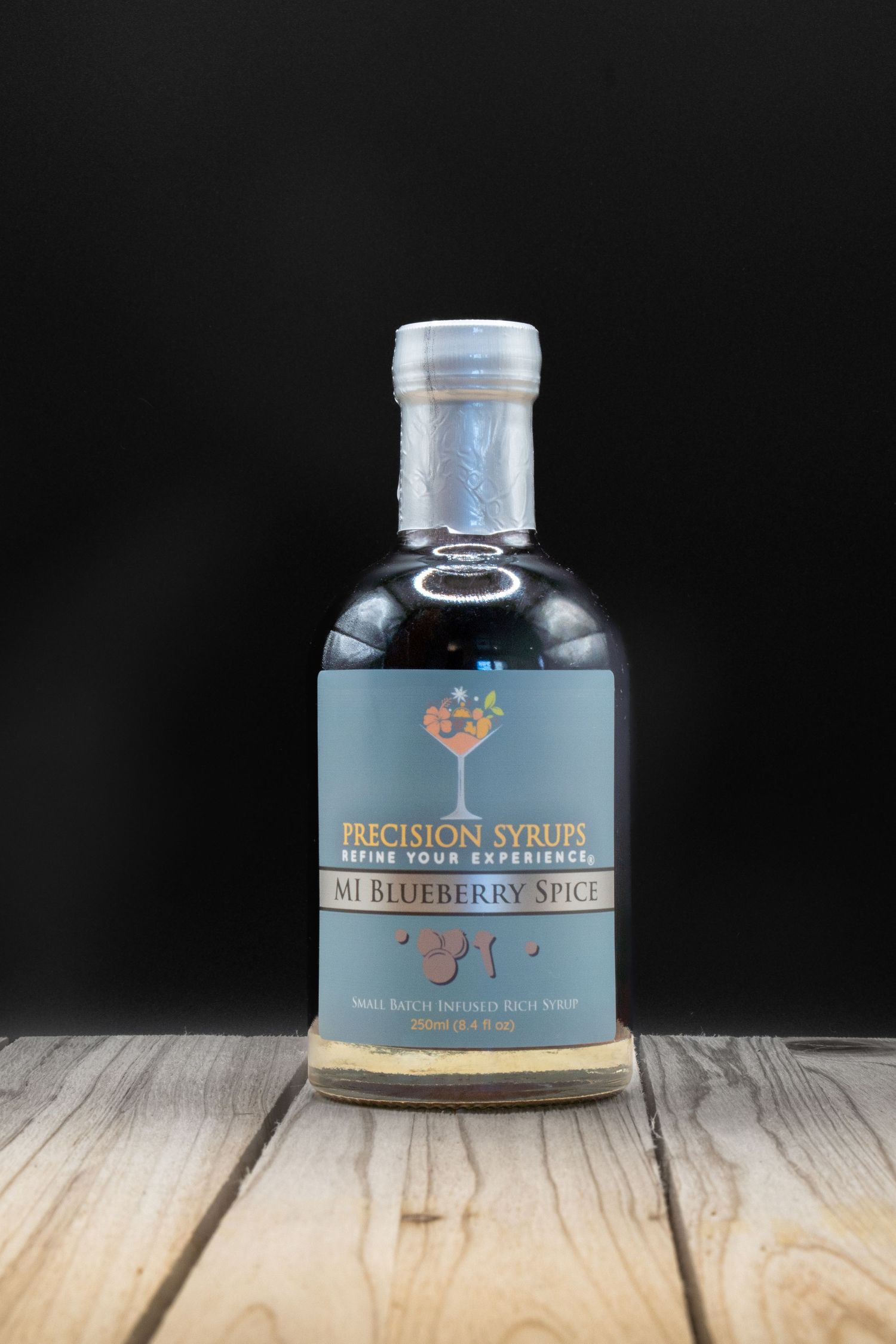 A bottle of blueberry syrup from Precision Syrups on rustic wooden surface.