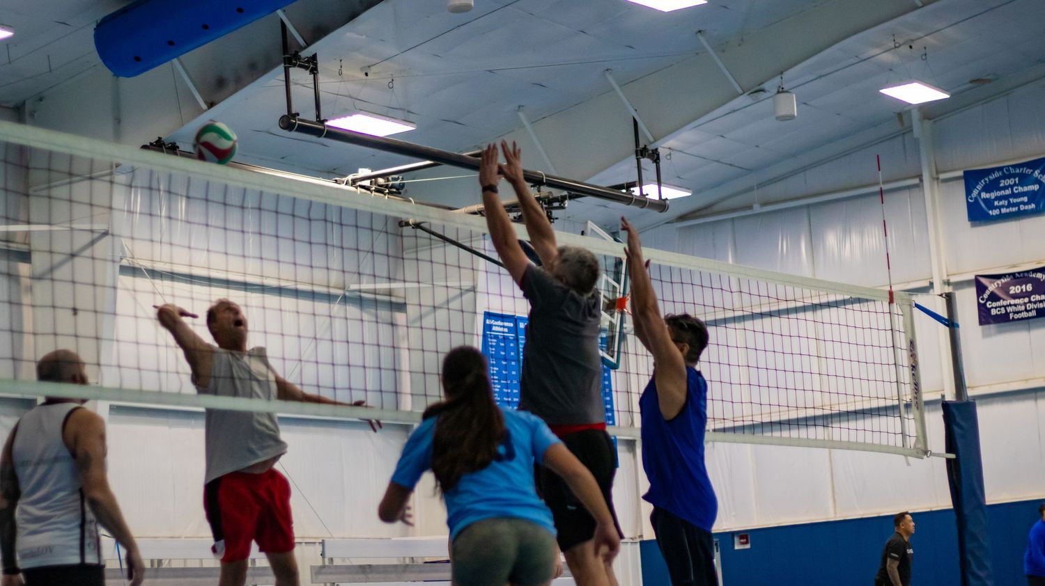 Volleyball players jump at net during competitive indoor match with multiple players in action.