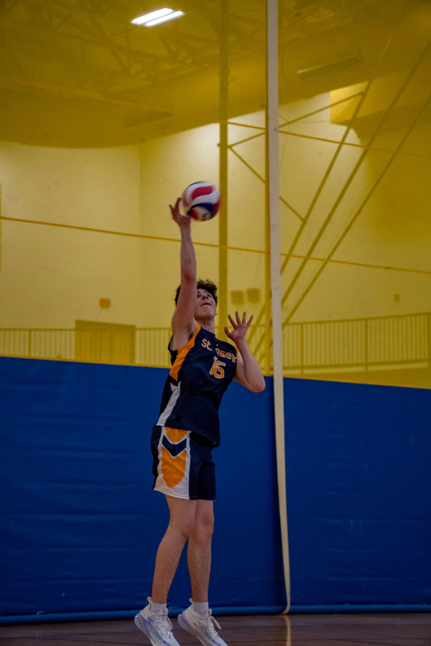 Player in navy uniform serving volleyball with perfect form in indoor gymnasium.