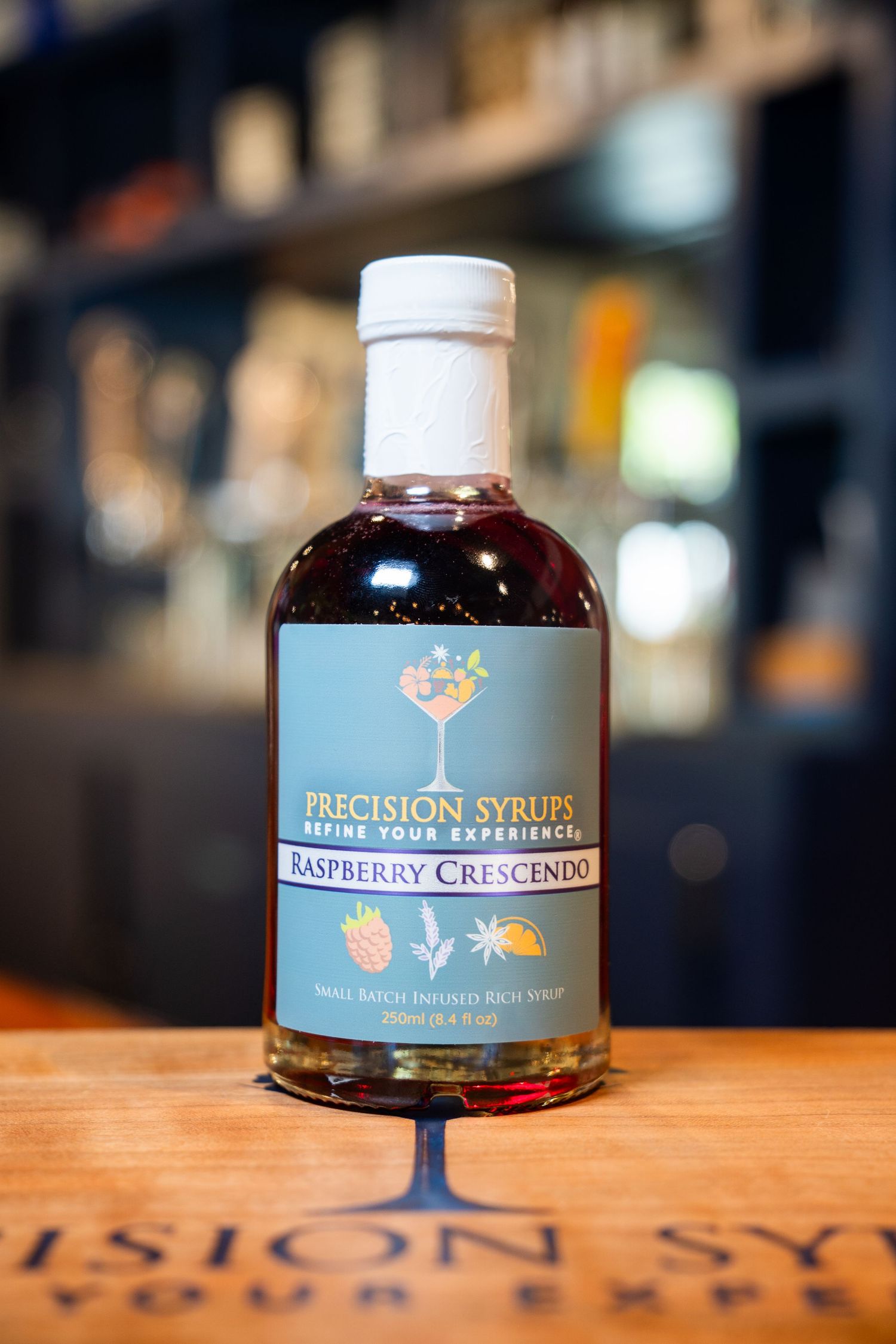 Bottle of Precision Syrups raspberry crescendo mixer on branded wooden surface.