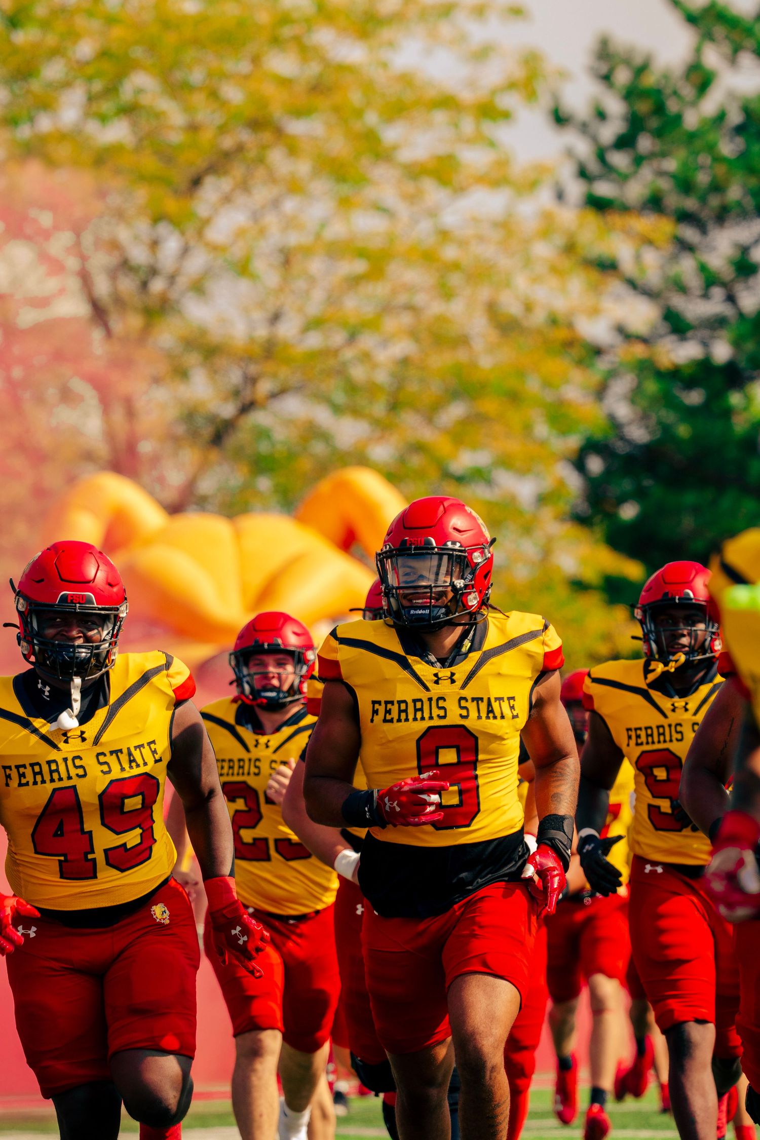 Football players in red and yellow uniforms line up in formation during practice on an autumn day.