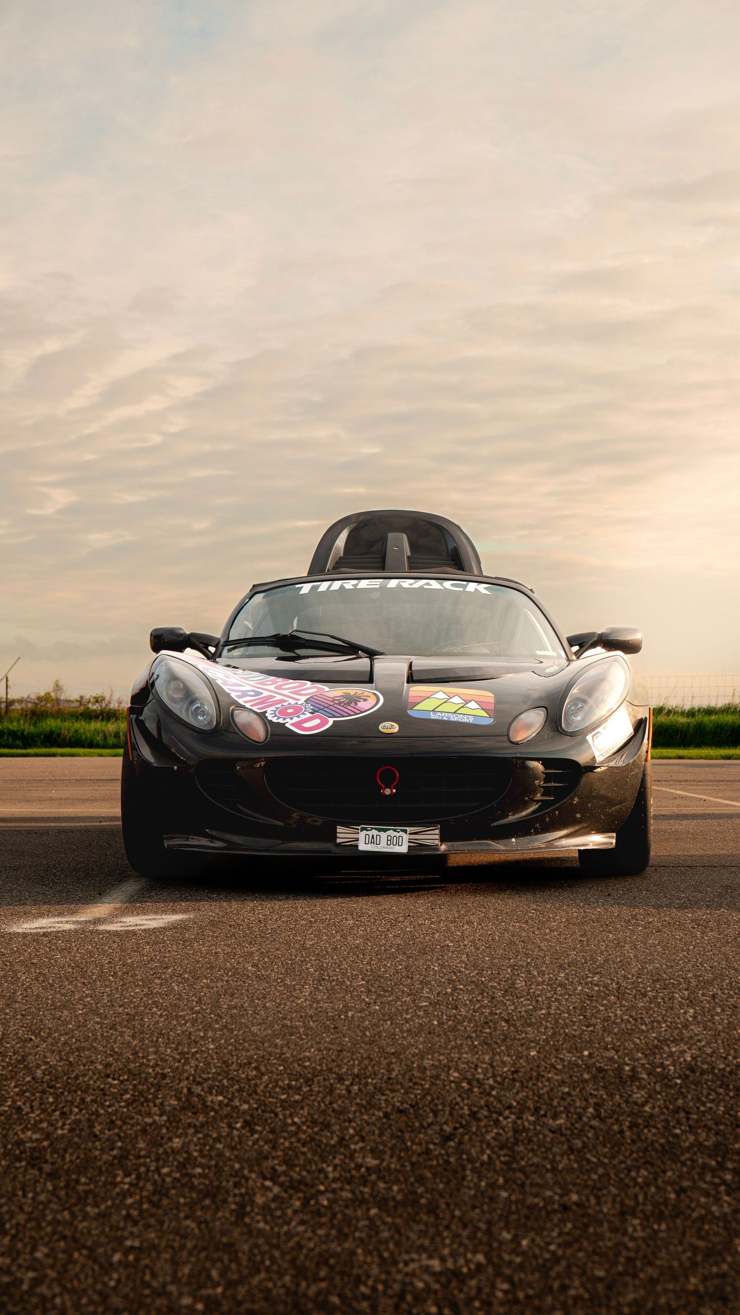 Front view of black Lotus race car on asphalt under cloudy sunset sky.