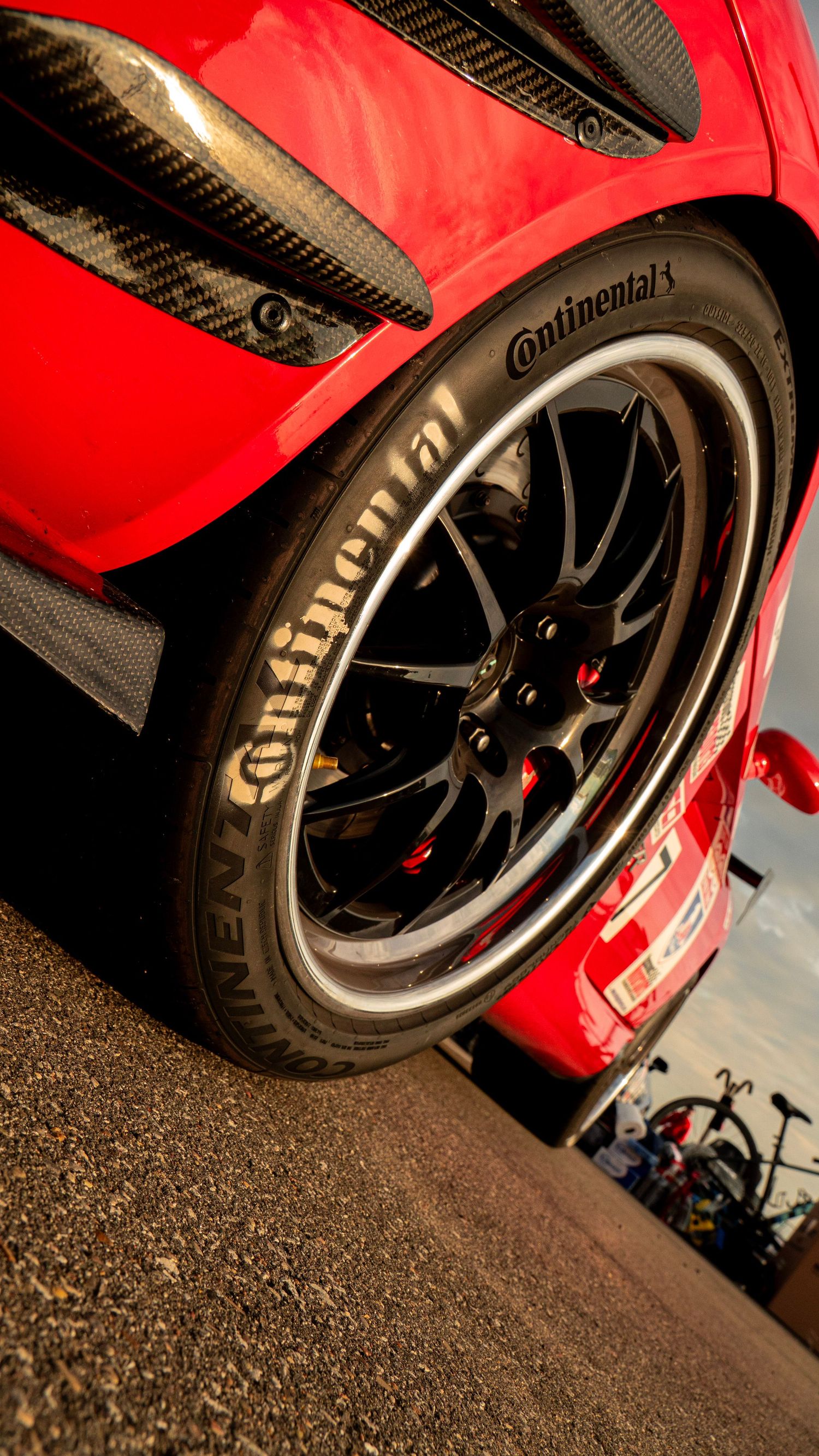Detail shot of red sports car with carbon fiber elements and black Continental racing wheels.