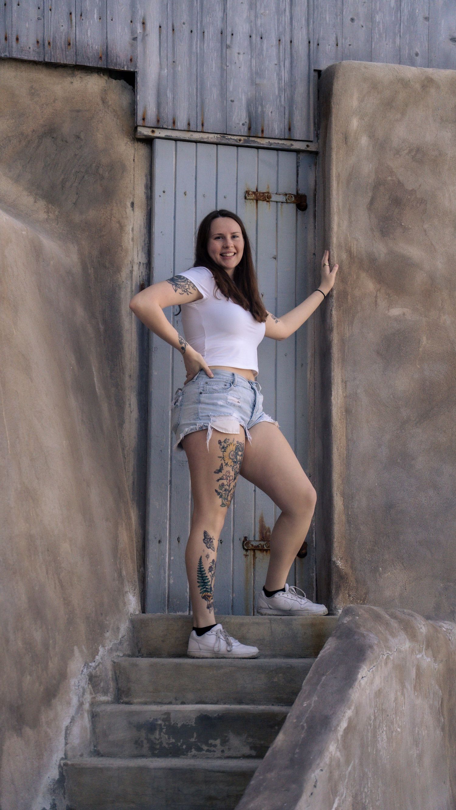 Model in casual summer attire poses on concrete steps against weathered blue door.